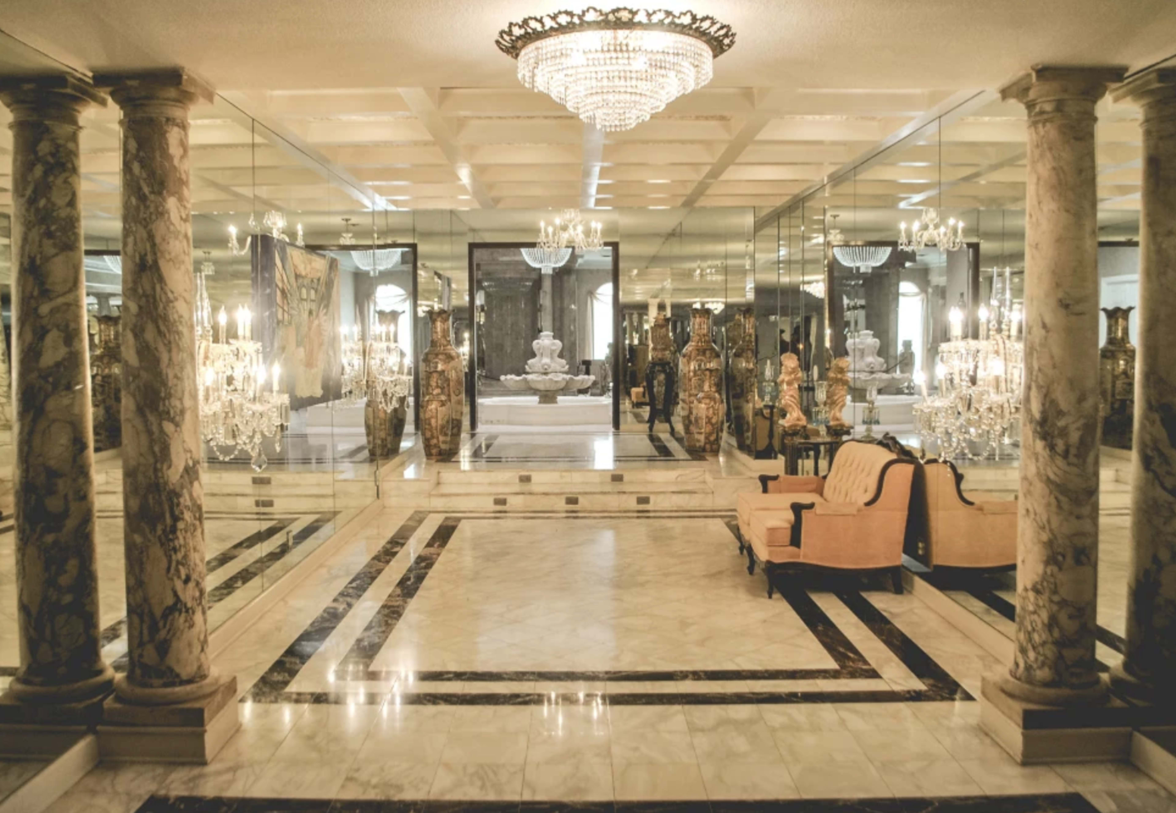 An opulent room featuring marble flooring, mirrored walls, and elegant furnishings, illuminated by a large chandelier.