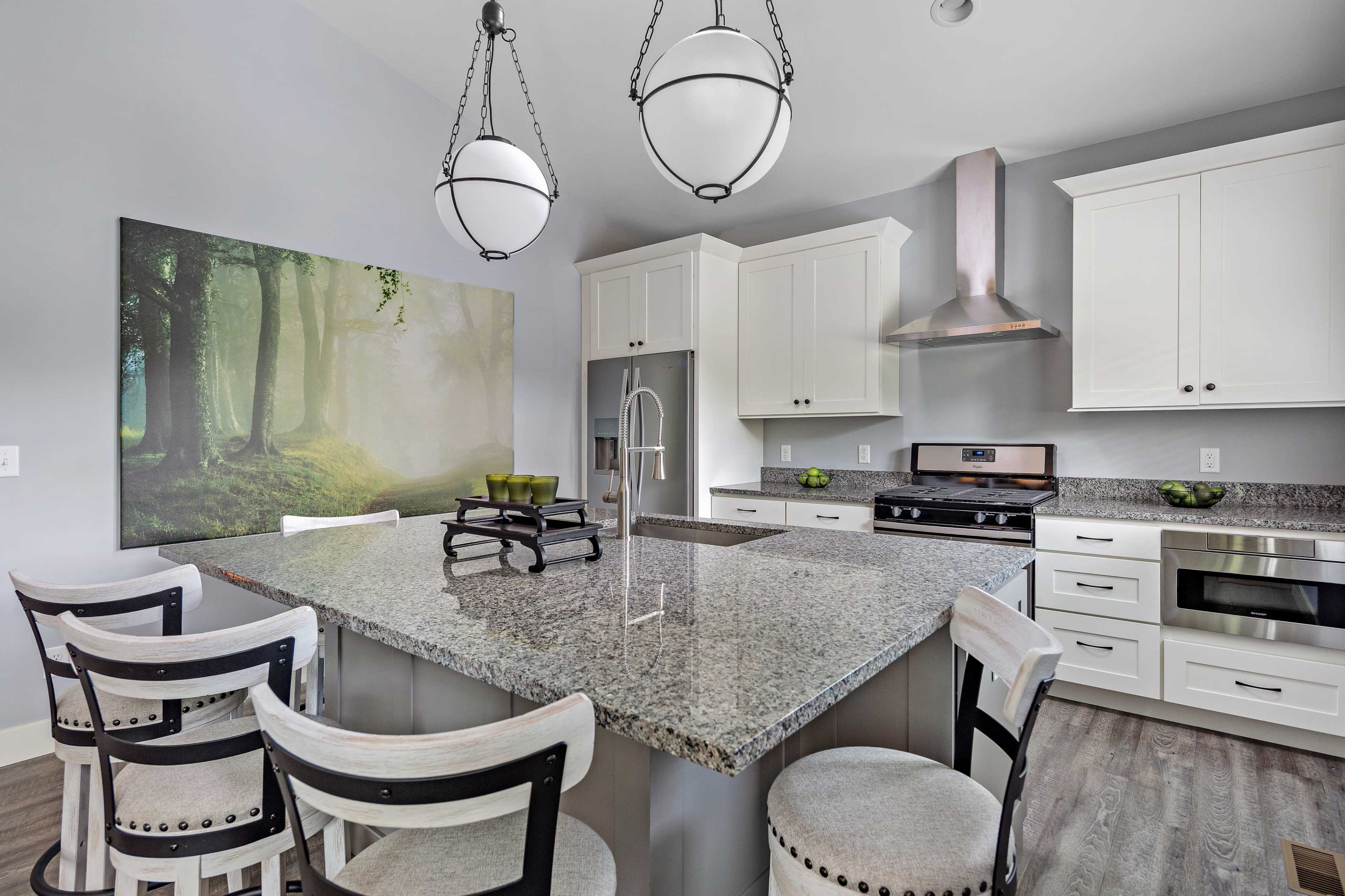 A modern kitchen with a large granite island, white cabinetry, and a wall mural of a forest.