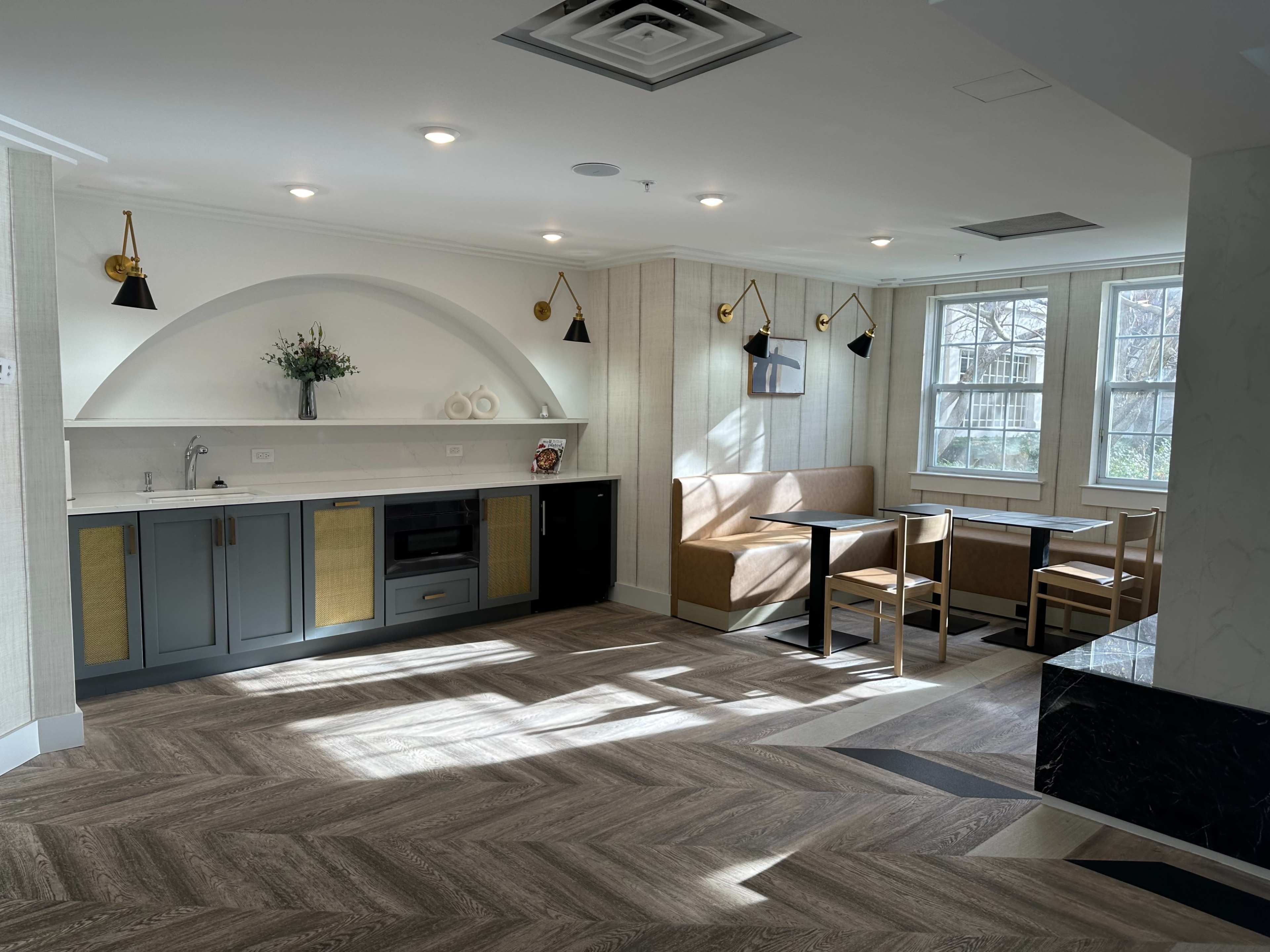 A modern kitchen and dining area with a gray counter, wooden seating, and large windows allowing natural light.
