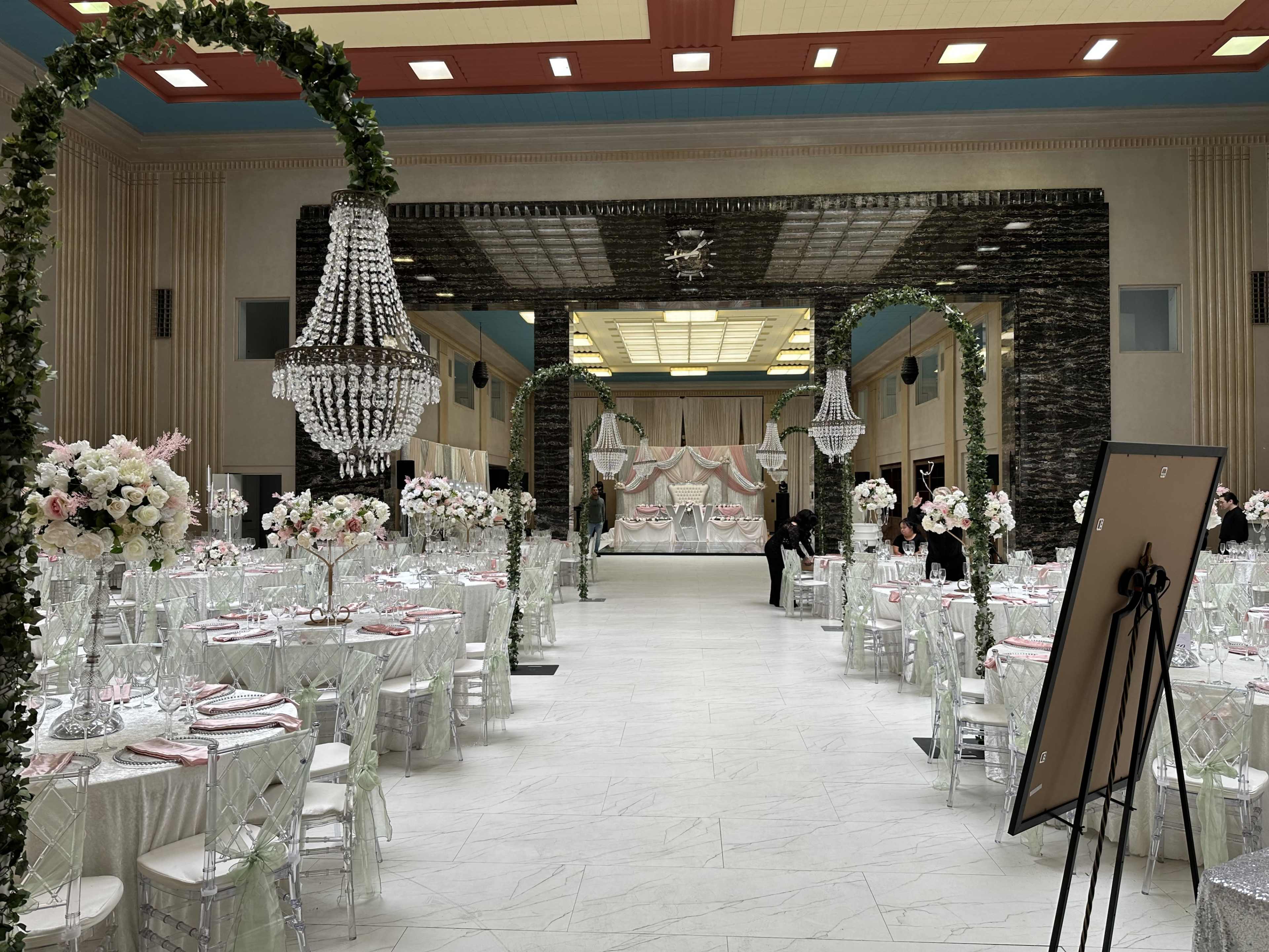 The image shows an elegantly decorated banquet hall with tables set for a formal event, adorned with floral centerpieces and chandeliers.