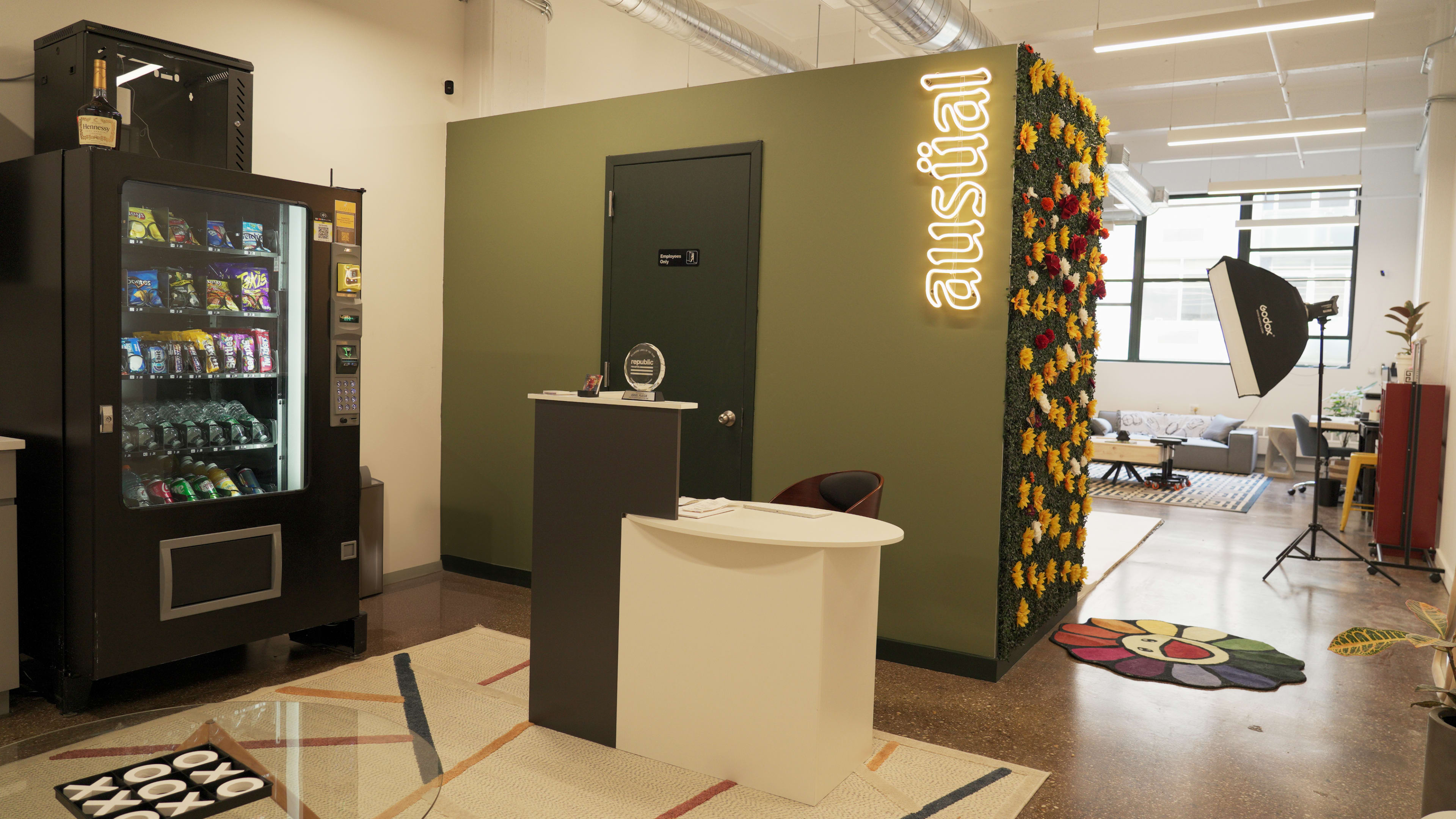 A modern office reception area with a vending machine, a check-in counter, and a wall adorned with flowers next to a lounge area.