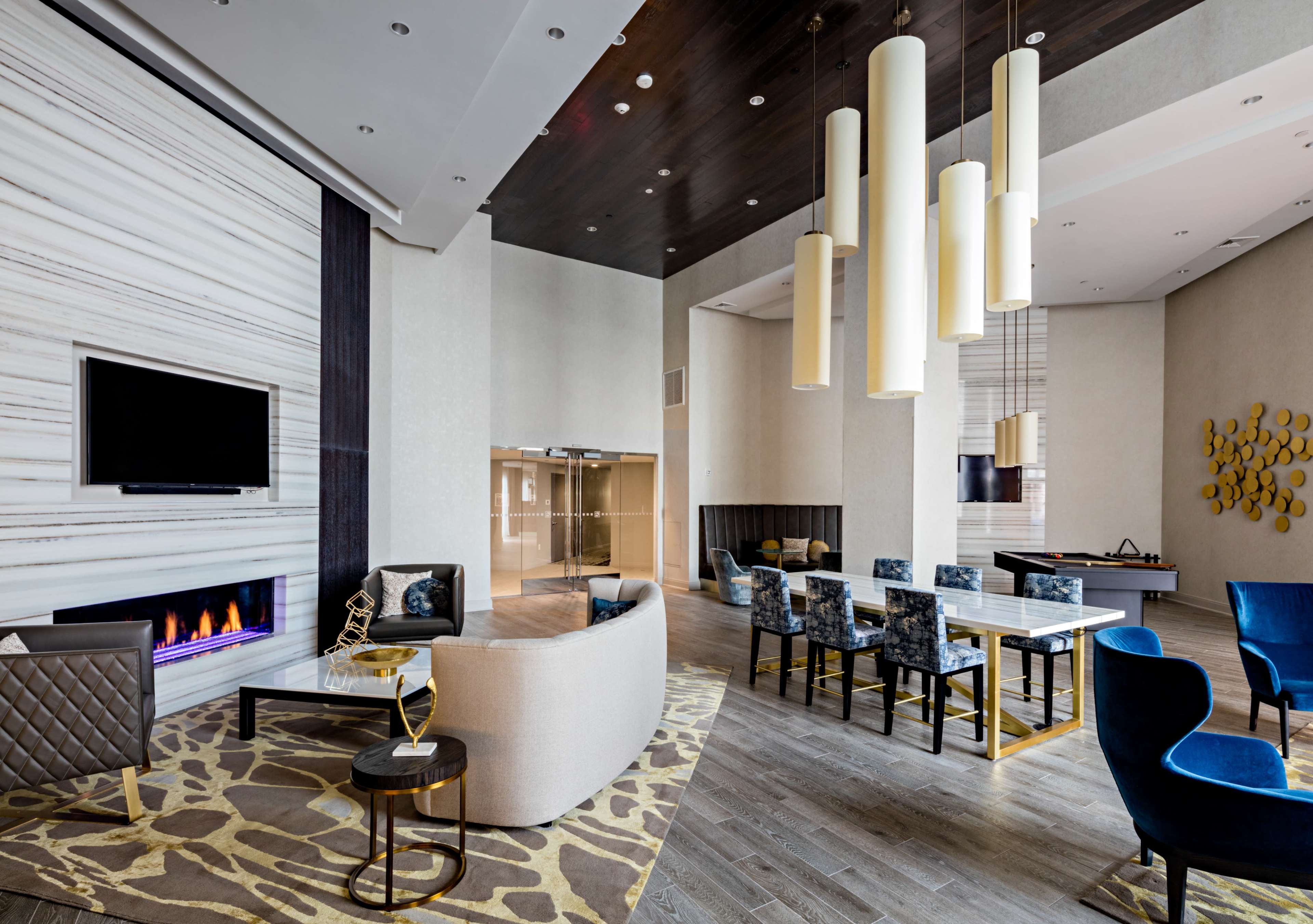 A modern lounge area features a fireplace, a large television, various seating arrangements, and a dining table.