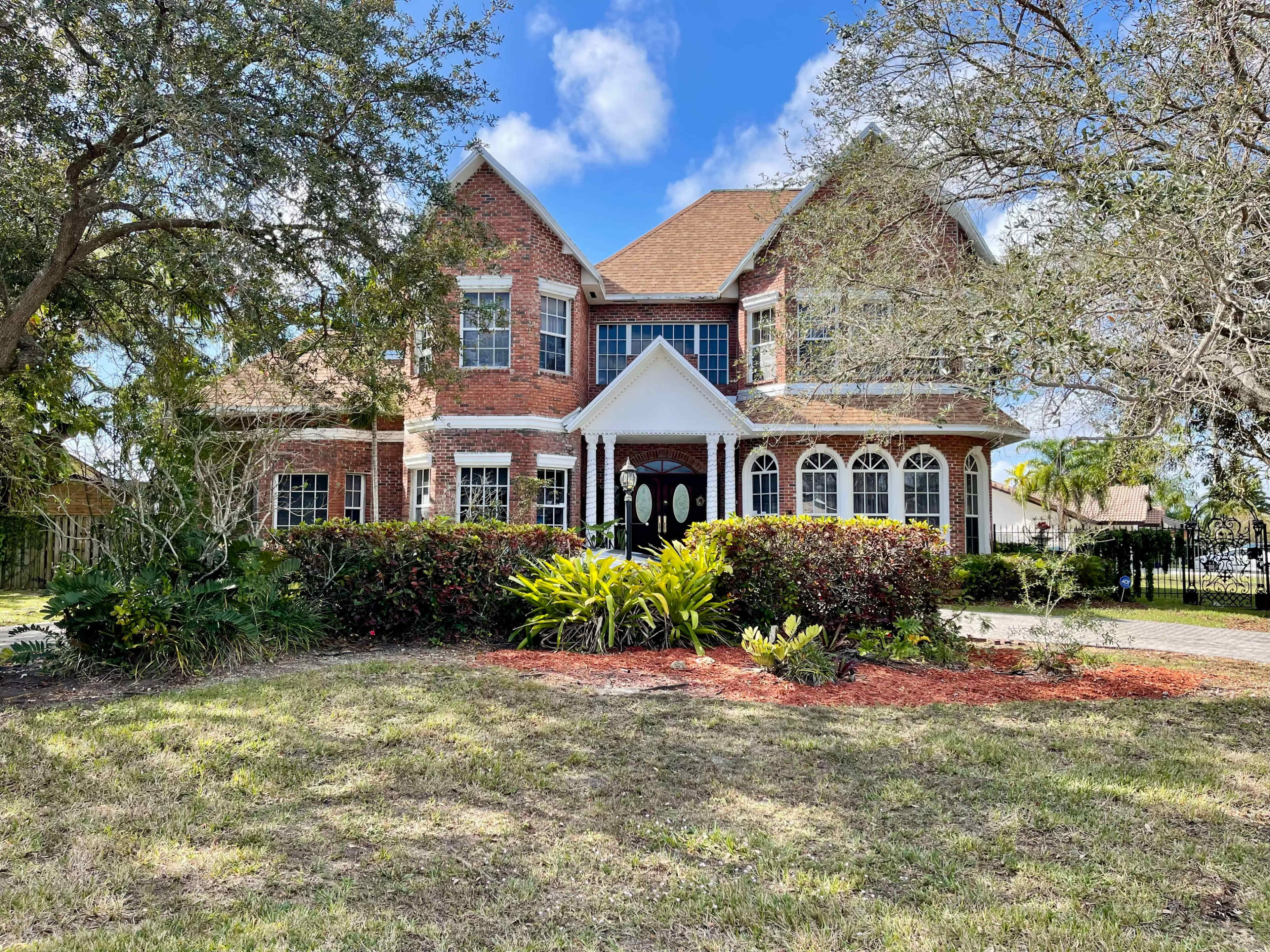 A large, two-story brick house with a manicured front yard and flowering shrubs.