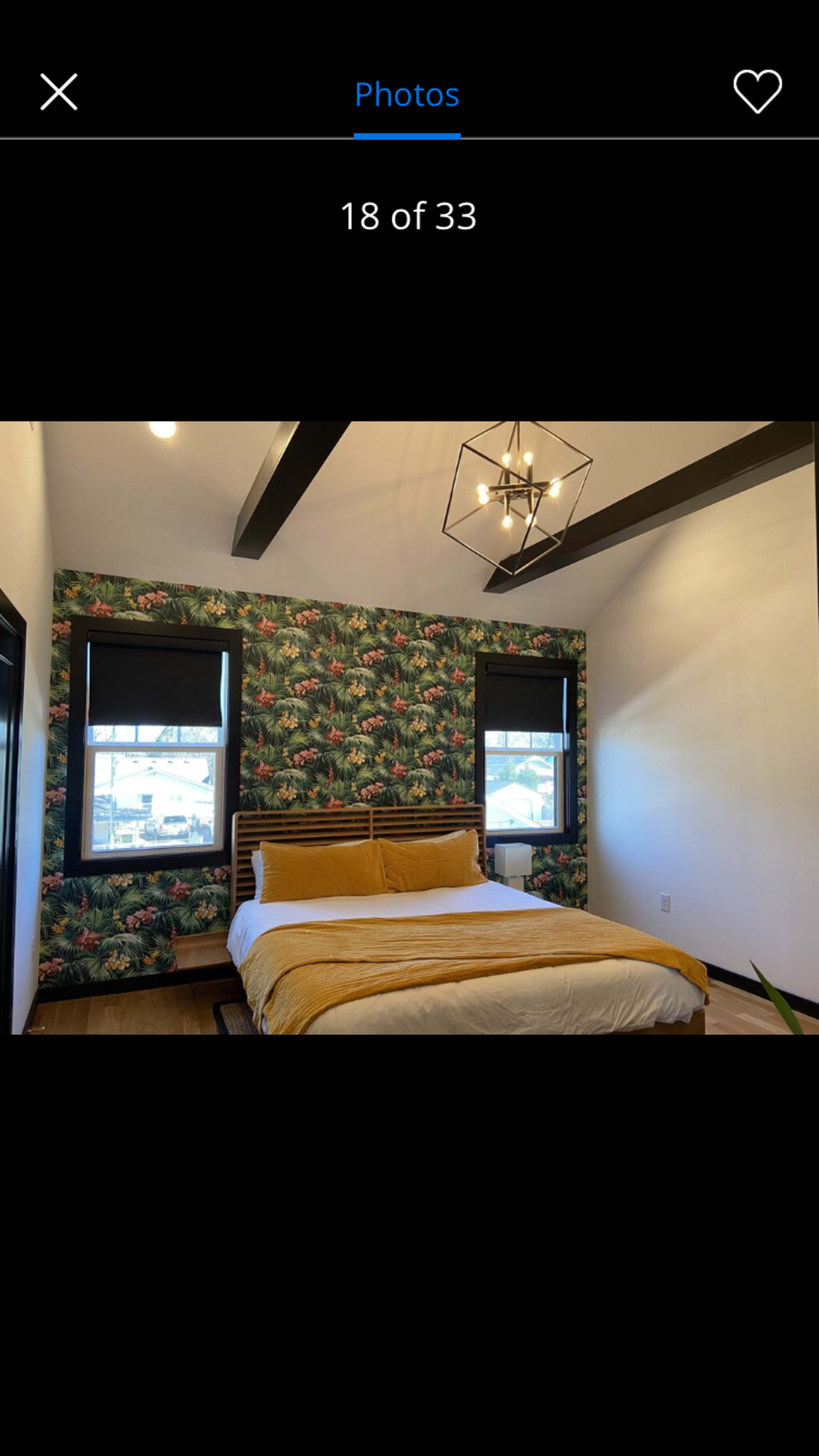 A bedroom with a bed covered in a yellow and white comforter, featuring a floral accent wall and large windows.