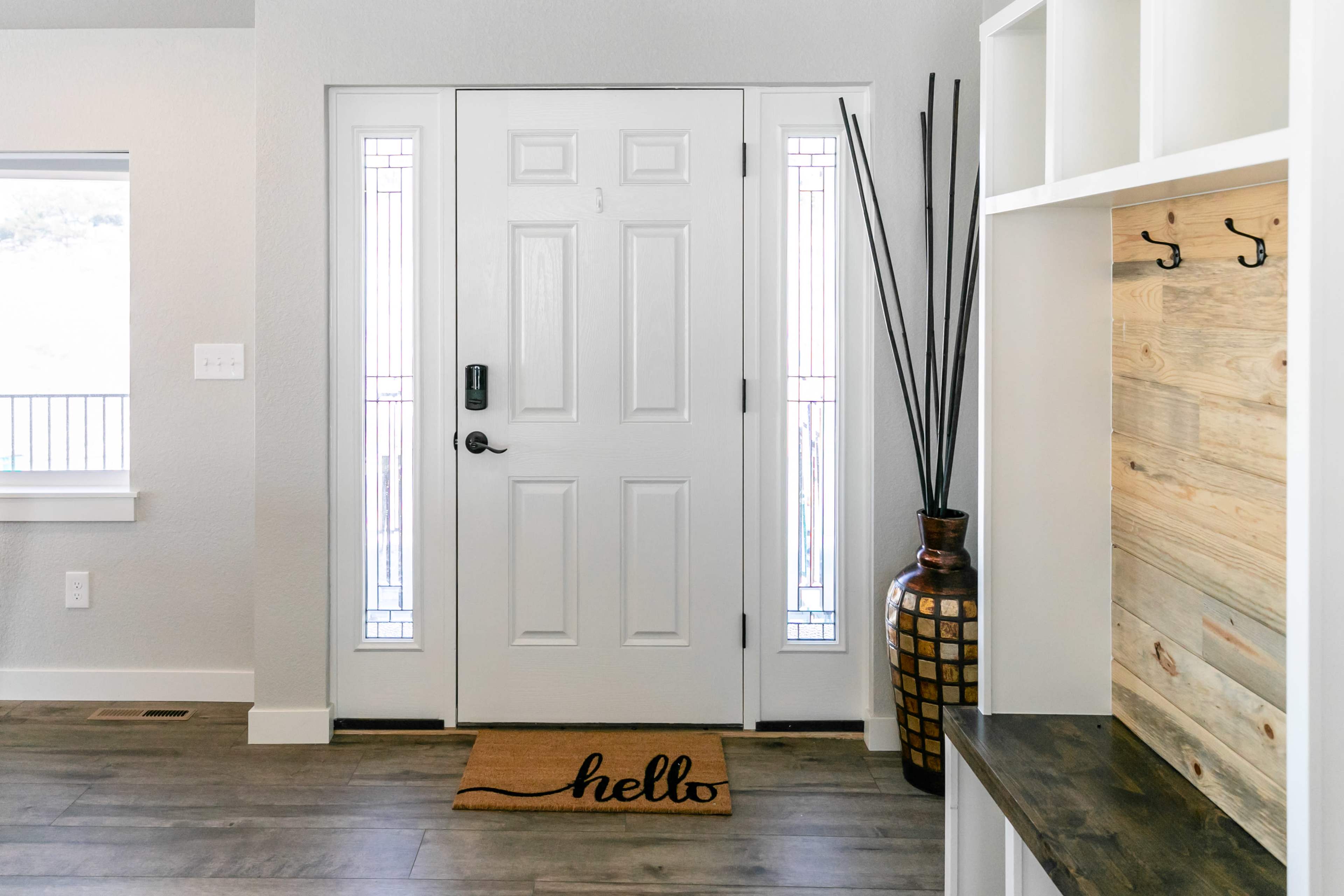 A modern entryway with a white door, decorative elements, and a "hello" doormat.