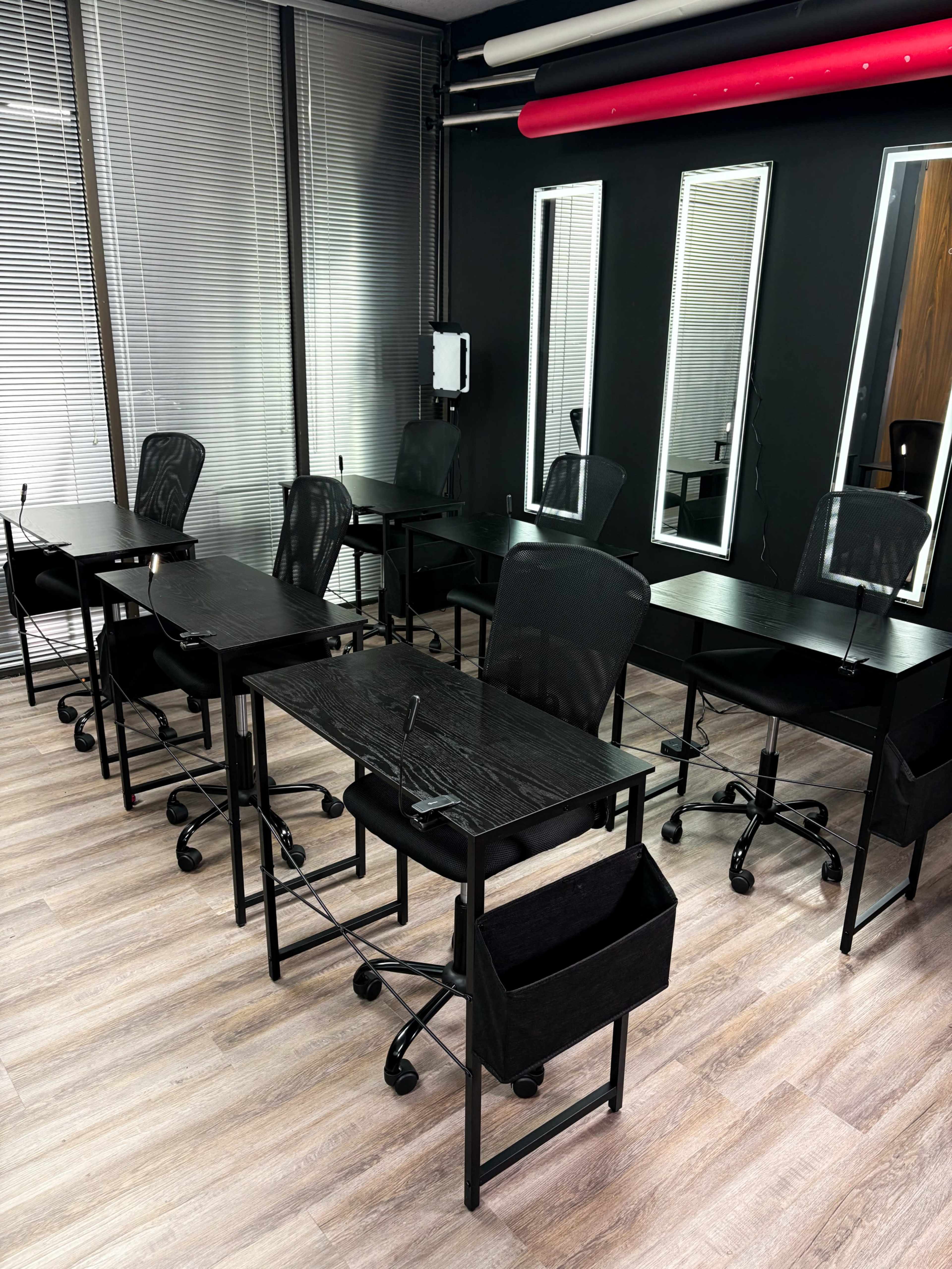 The image shows a modern workspace with several black desks and chairs arranged in a room featuring large windows and mirrors.