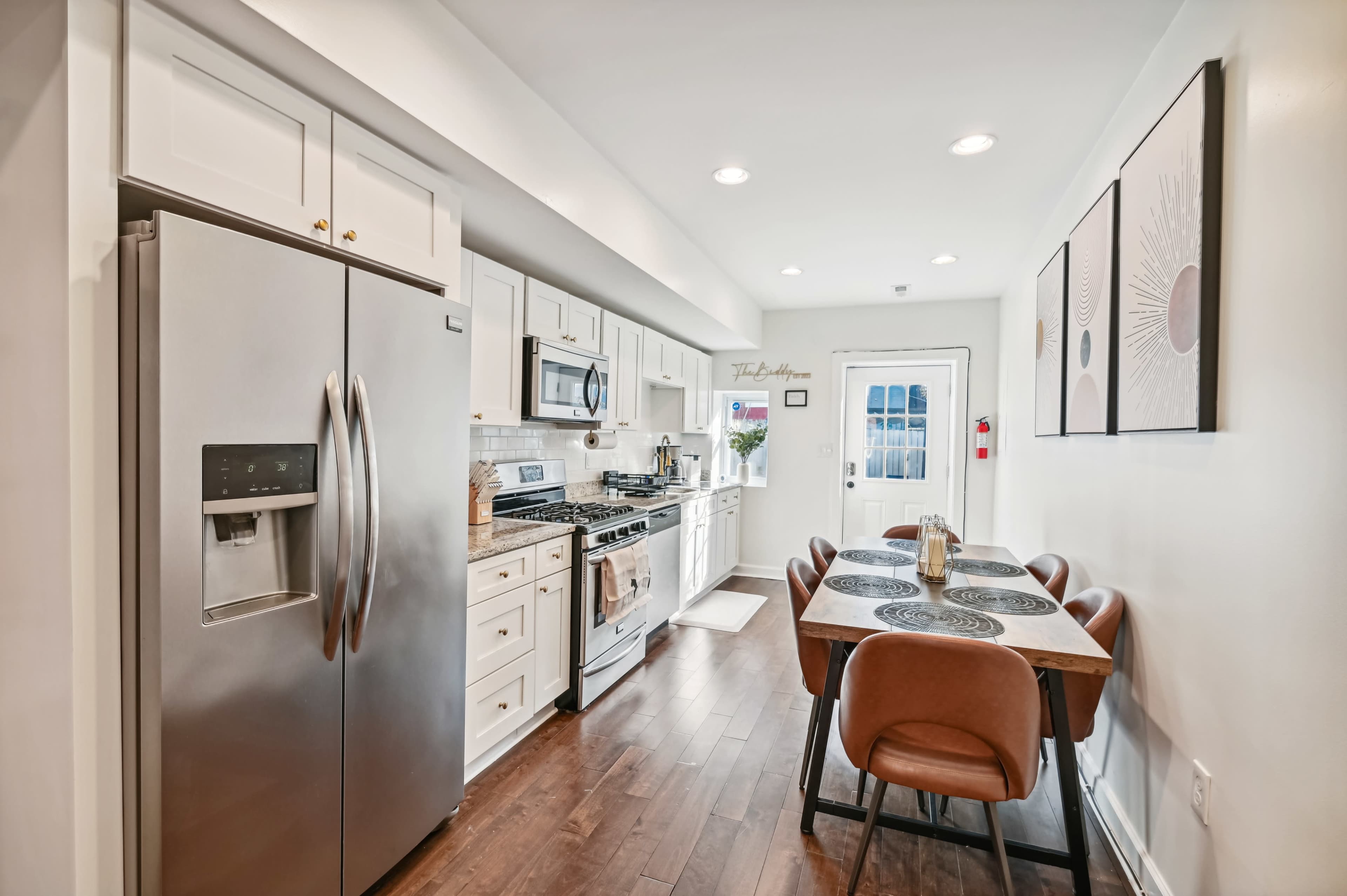 A modern kitchen features stainless steel appliances, white cabinetry, and a dining table with brown chairs.