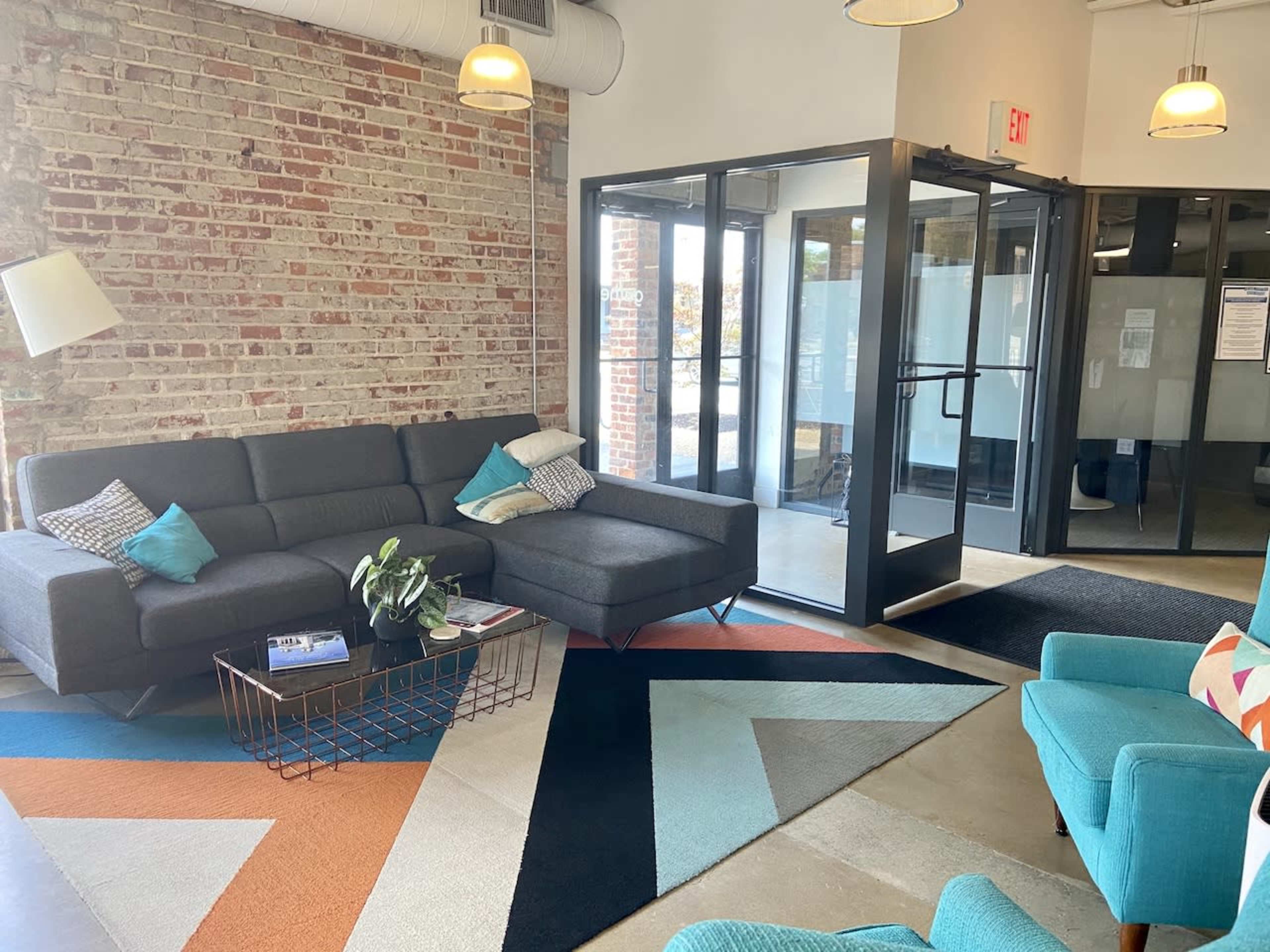 A modern lobby area with a gray sectional sofa, a geometric patterned rug, and glass doors leading outside.