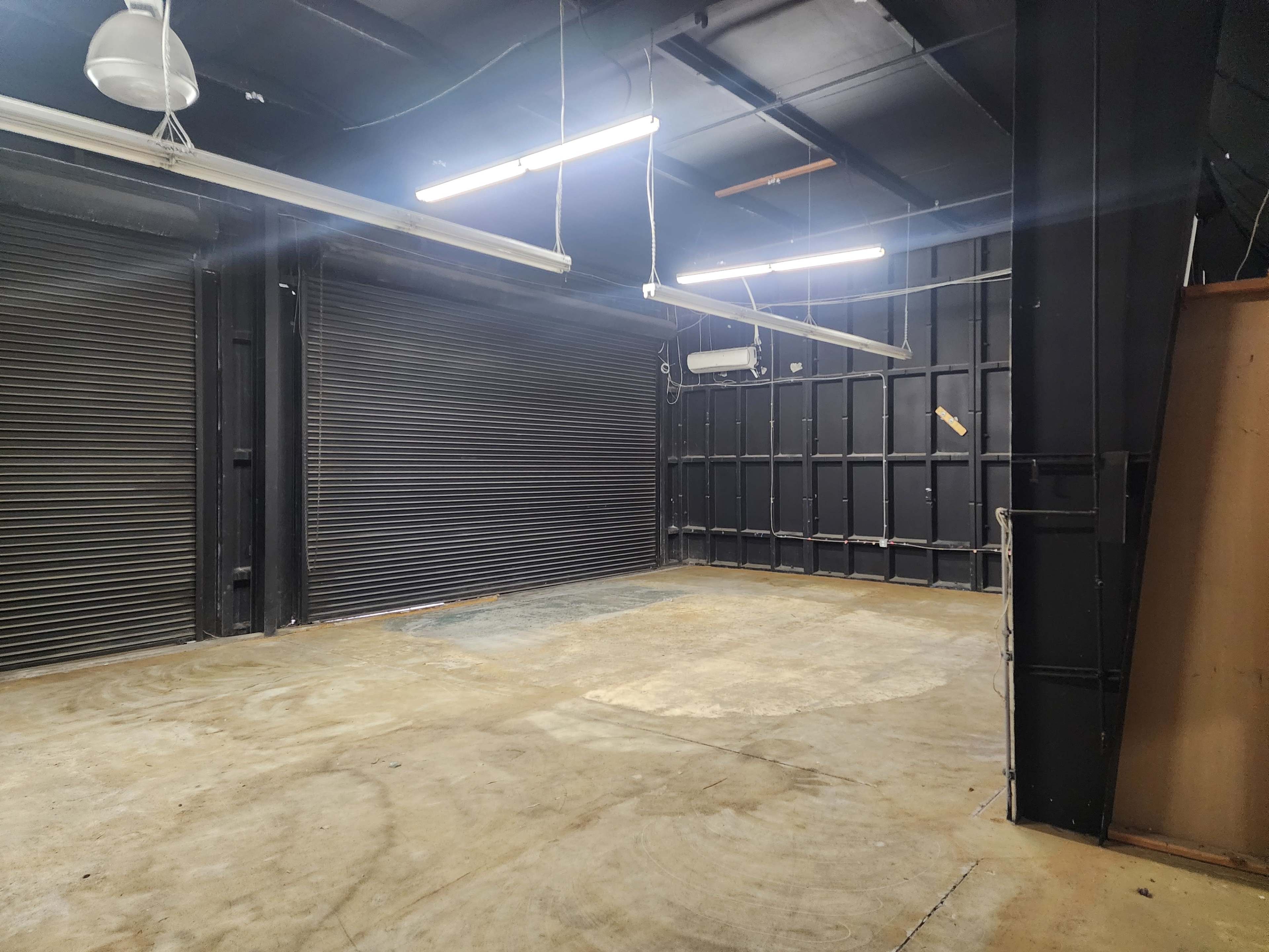The image shows an empty warehouse space with closed metal roll-up doors and exposed beams.