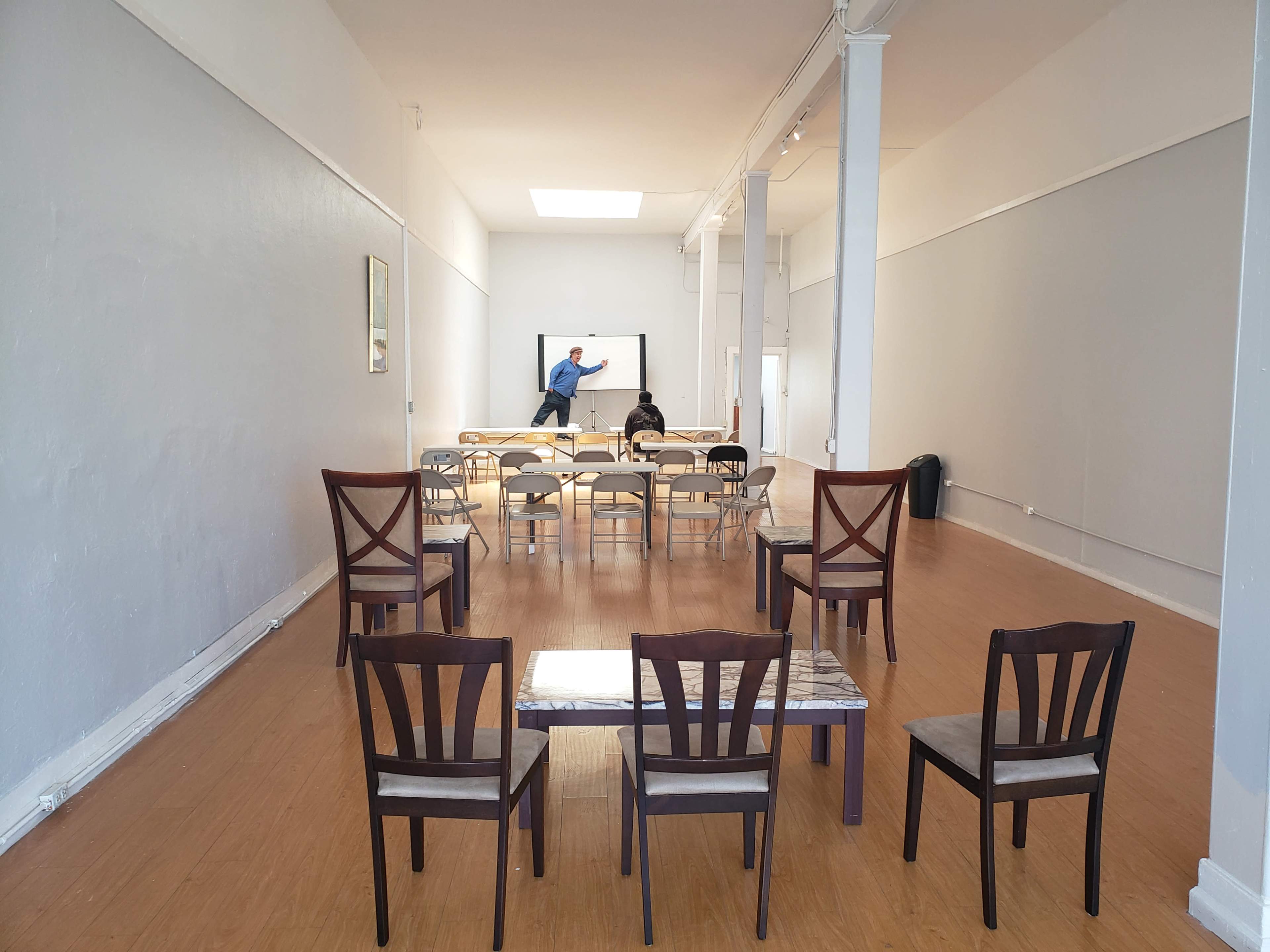 A spacious room with a row of chairs facing a whiteboard, where two people are engaged in a discussion.