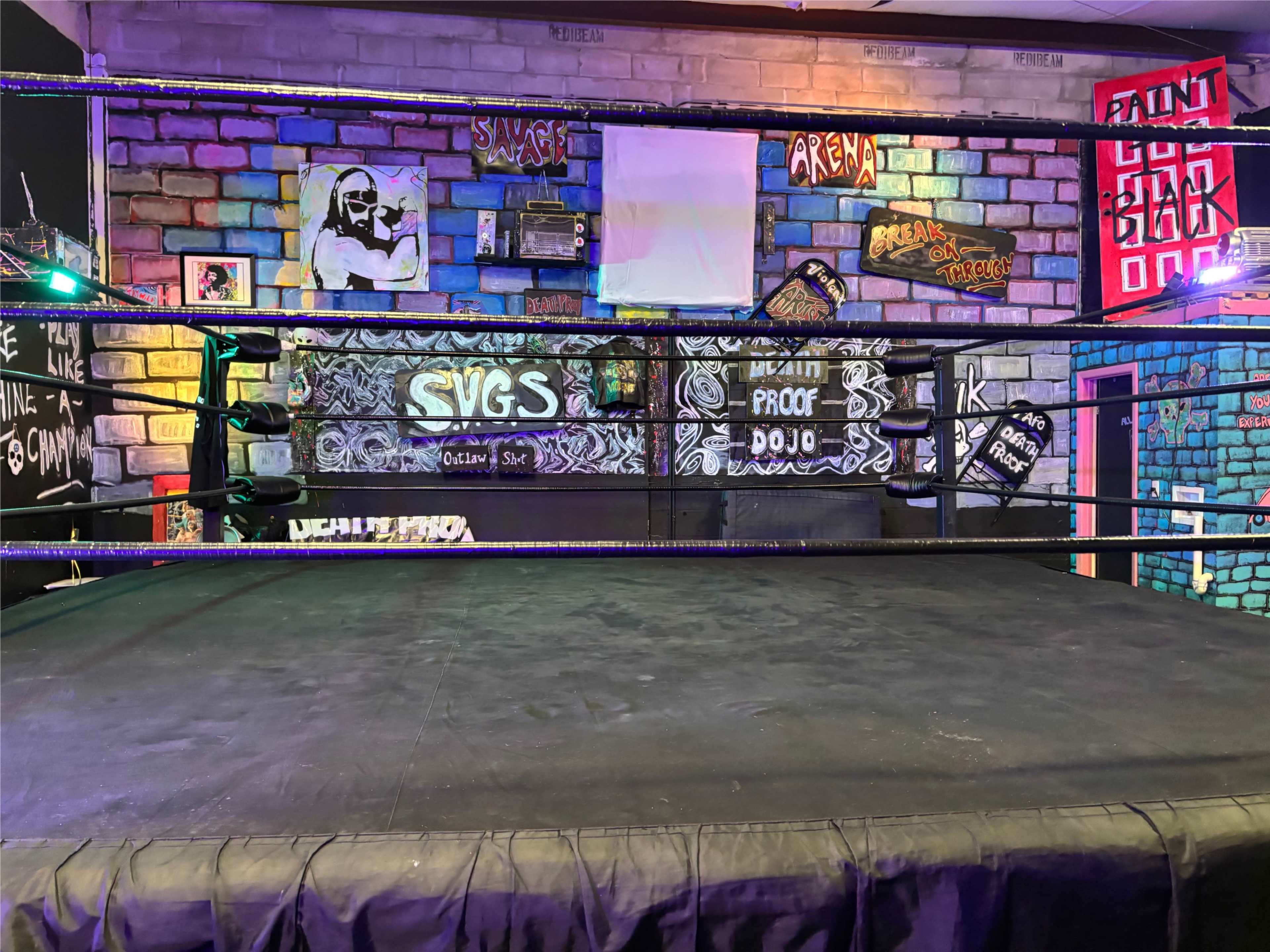 The image shows a wrestling ring situated against a colorful, graffiti-covered wall in an indoor arena setting.