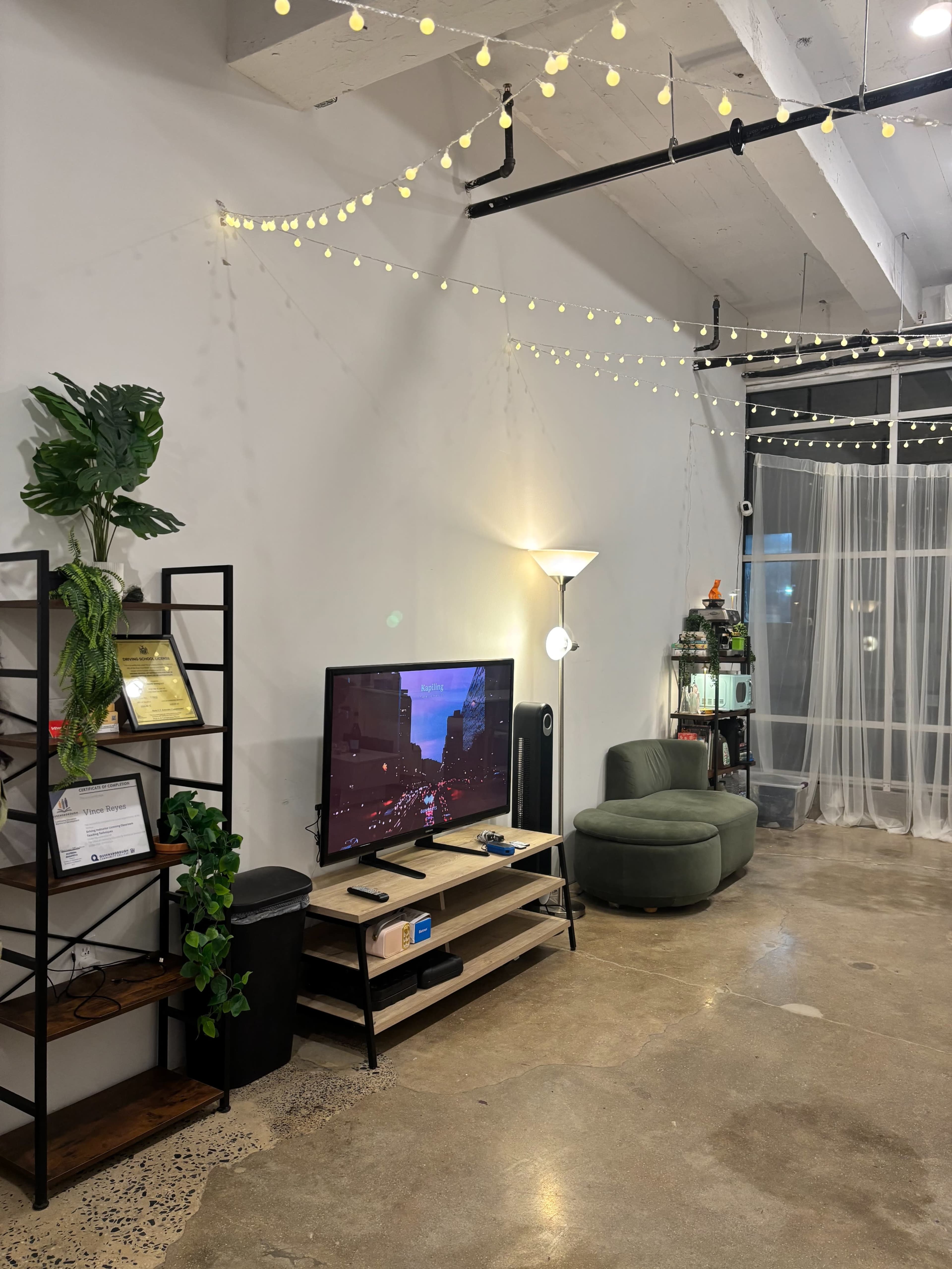 The image shows a modern living space with a television on a low stand, a green sofa, and decorative string lights hanging from the ceiling.