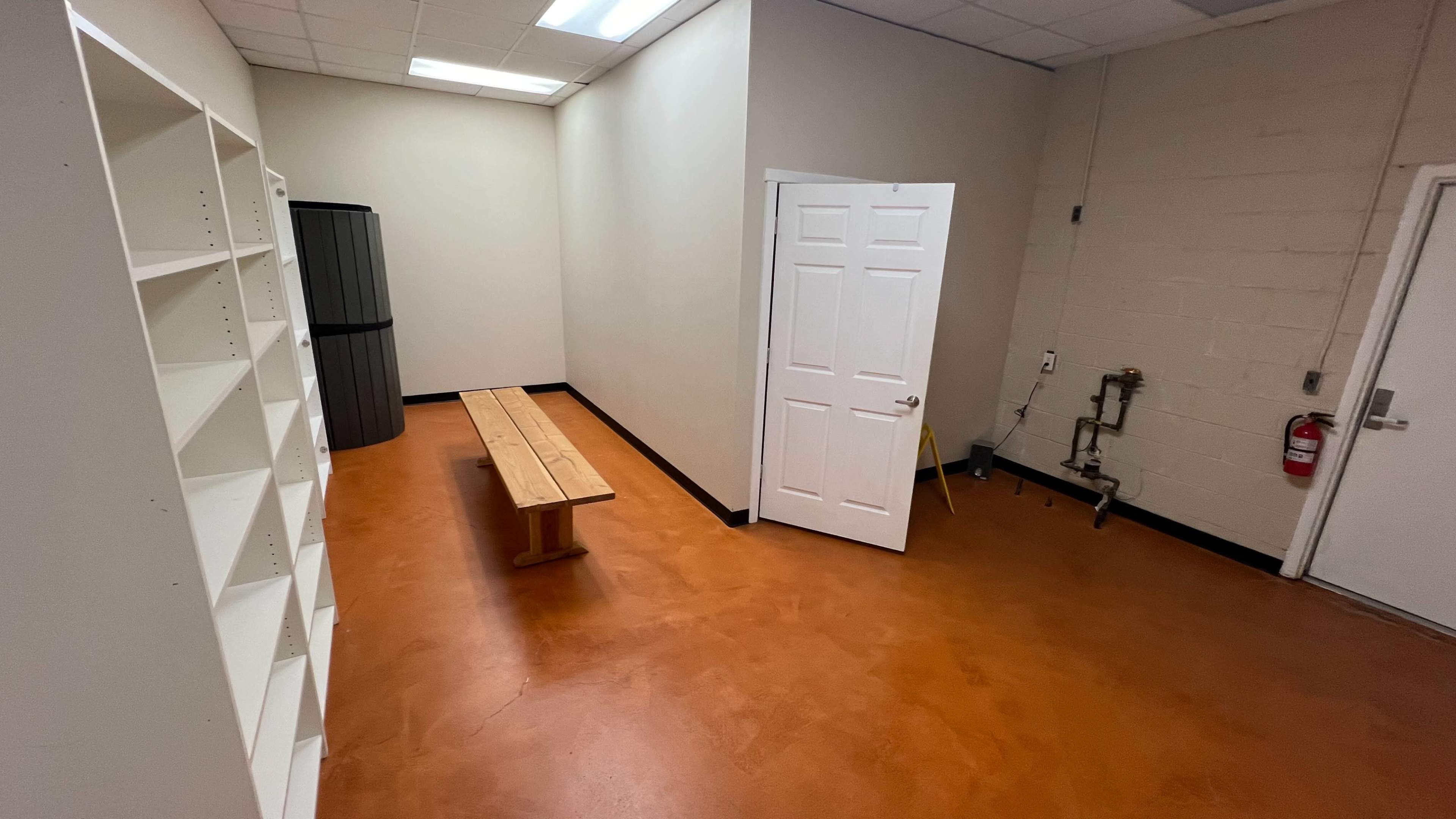 A small, empty room with a bench, shelf, and a door leading to another space.