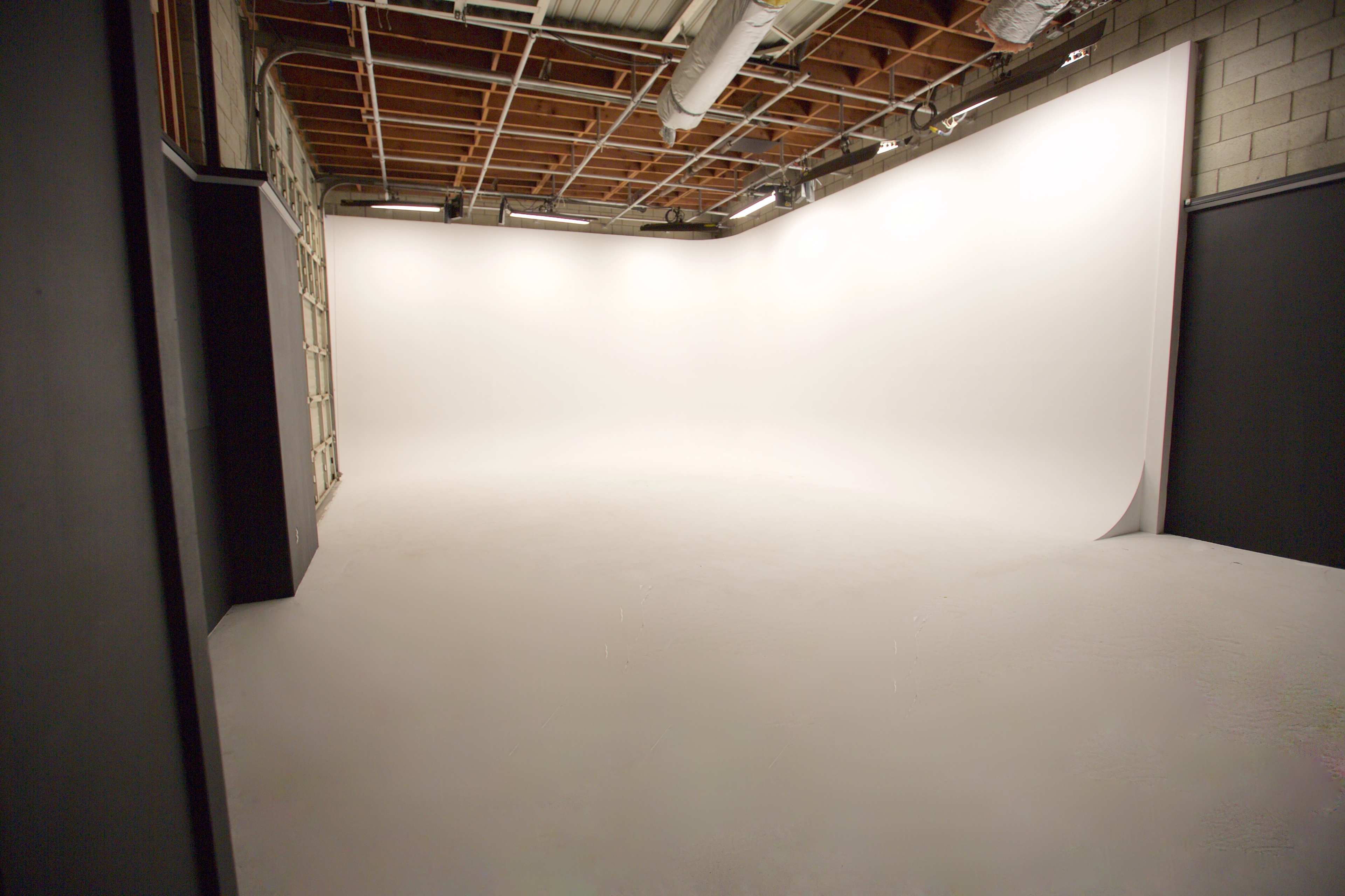 An empty photo studio with a seamless white backdrop and concrete walls.