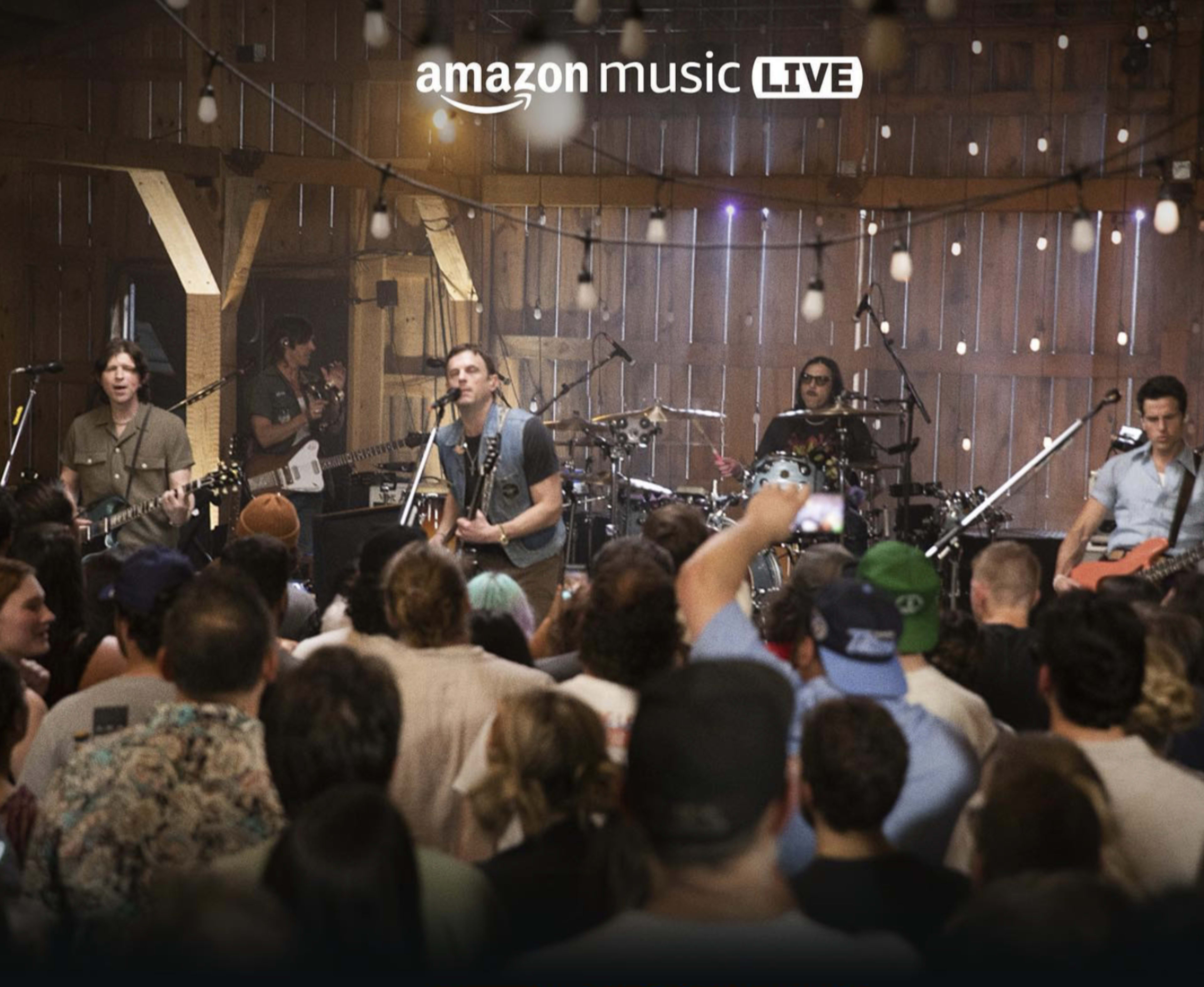 A band performs on stage in a rustic barn setting while an audience watches and enjoys the live music.