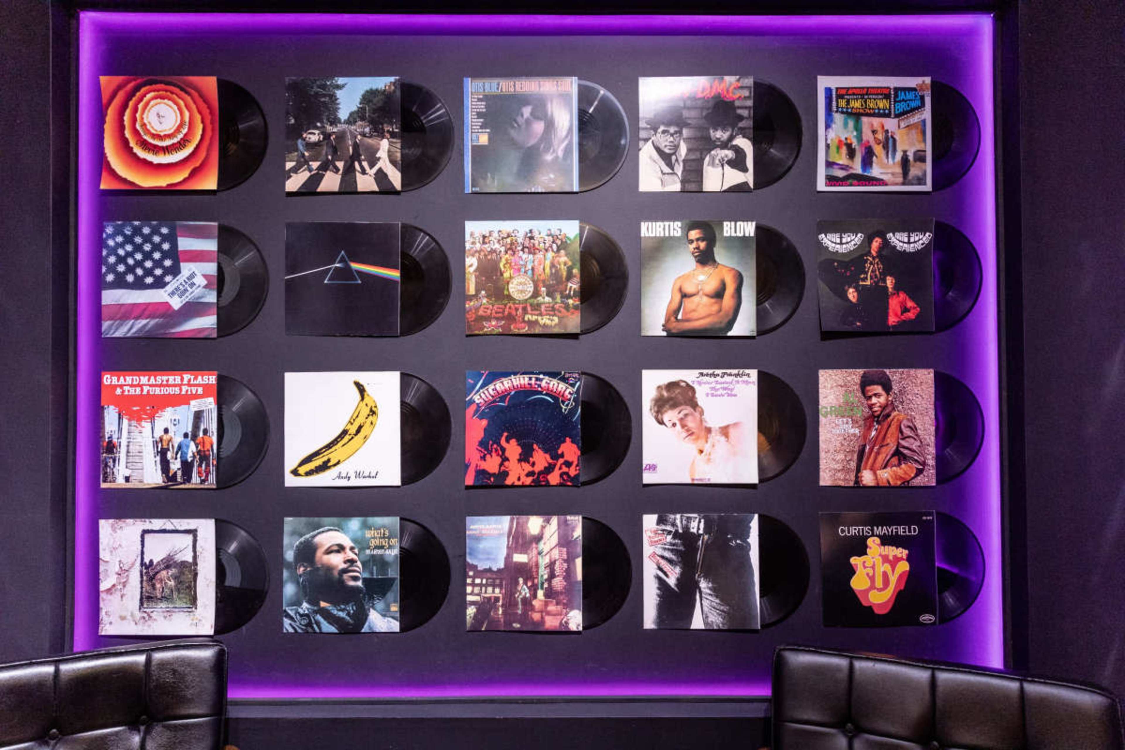 The image features a wall decorated with various vinyl records arranged in a grid pattern, set against a purple background.