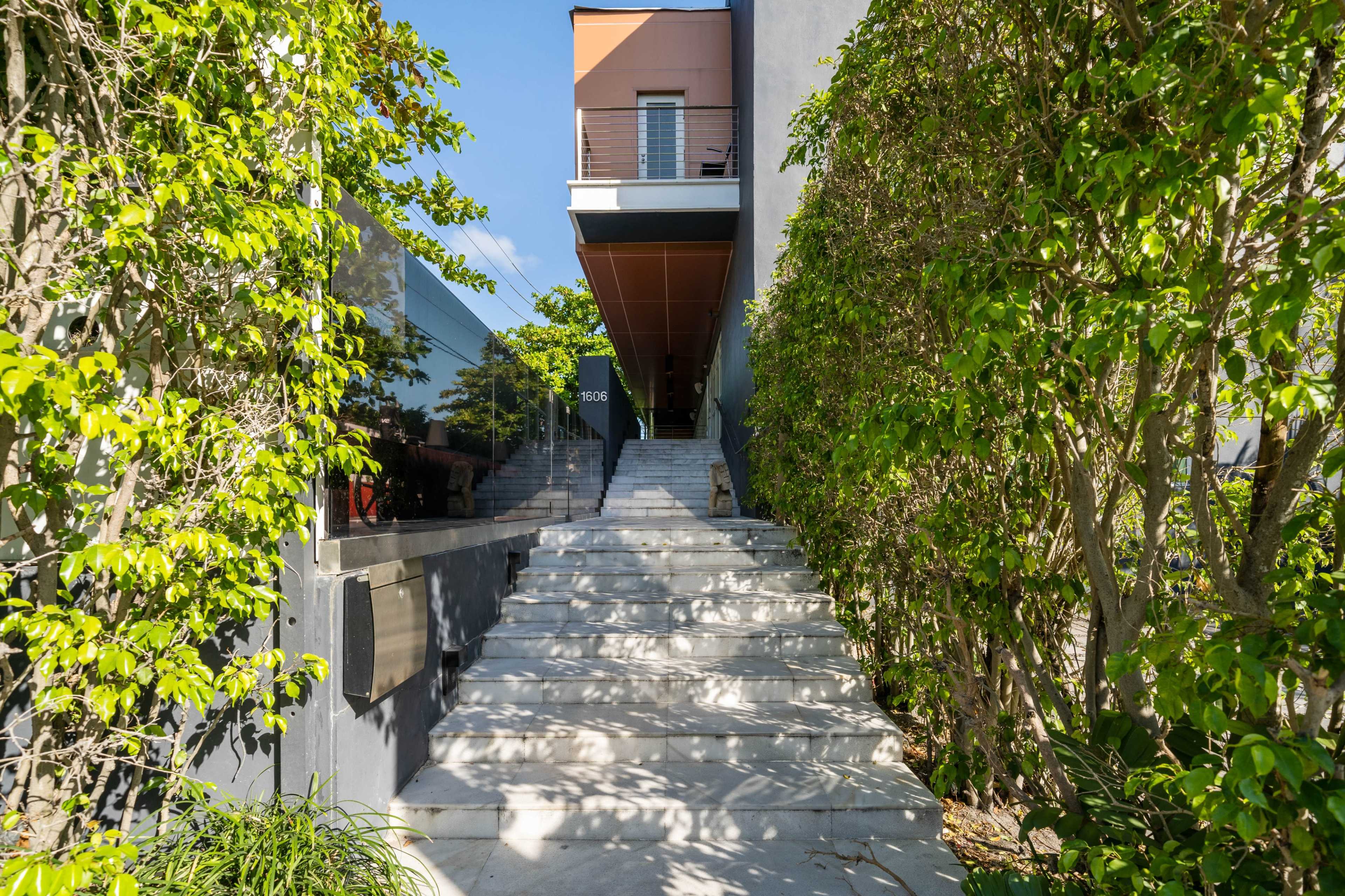 A stairway leads through greenery to the entrance of a modern building.