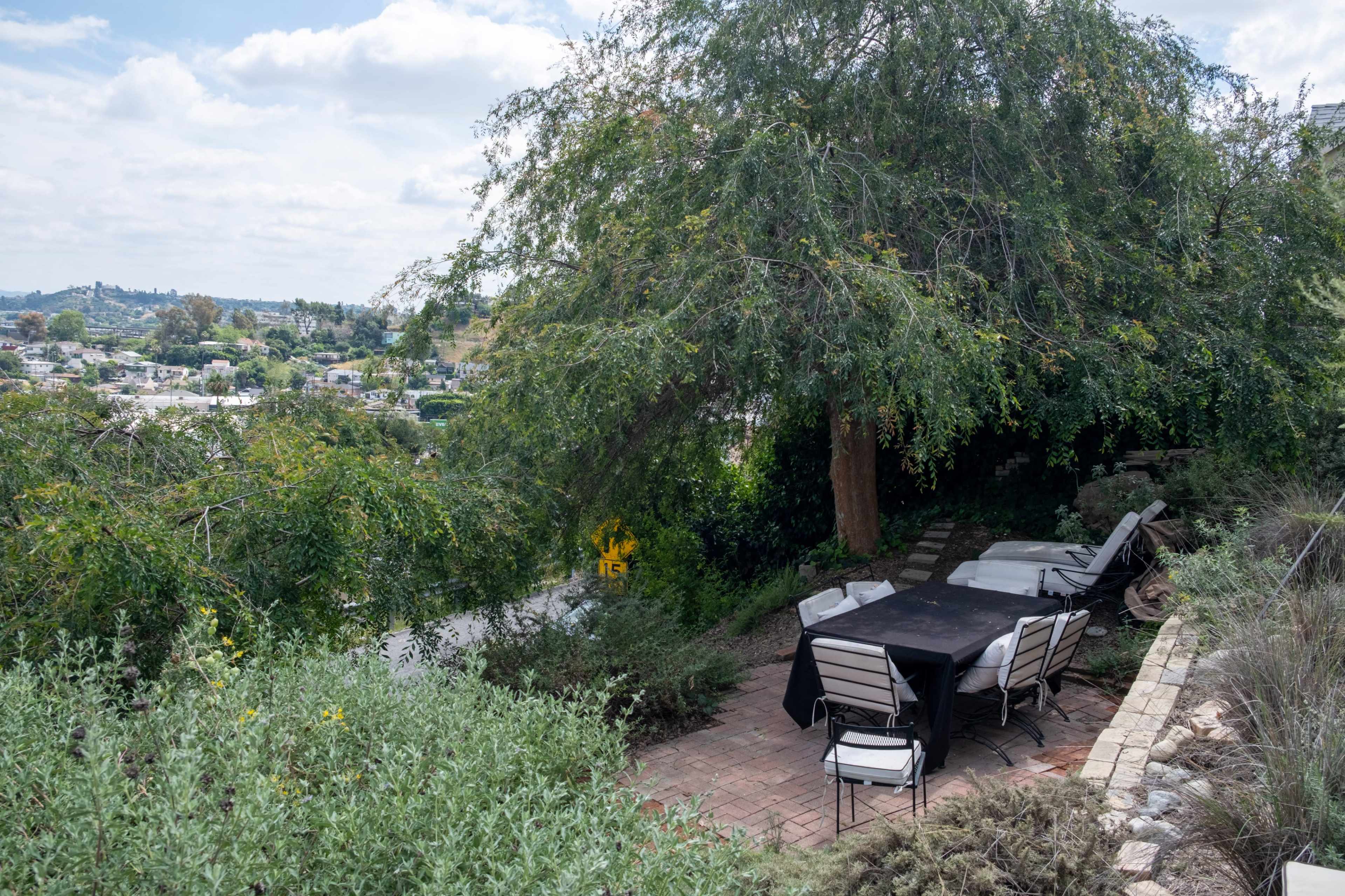 A patio with a black table and chairs is set against a backdrop of trees and a hillside view.