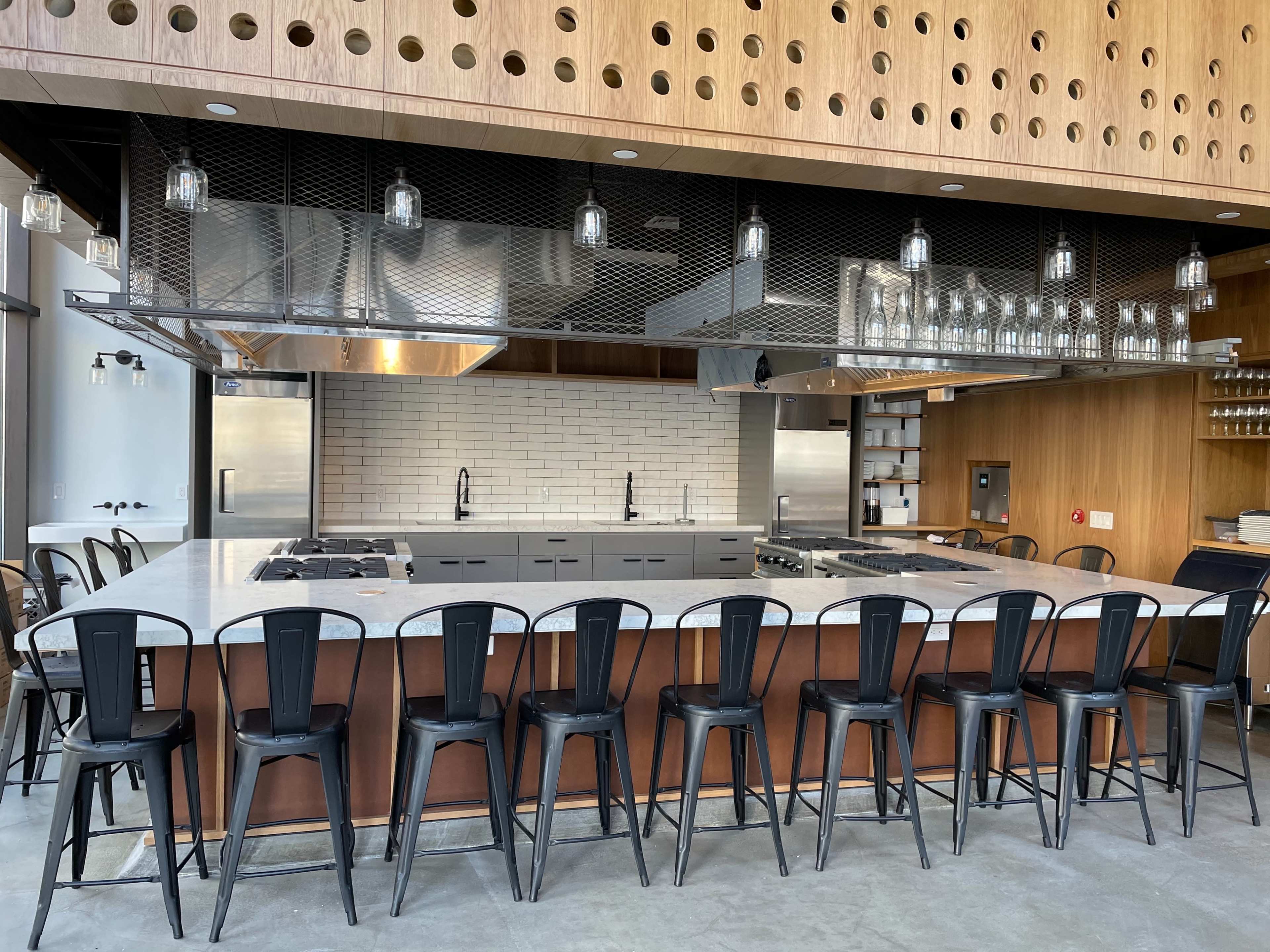 A modern kitchen with a large island, stainless steel appliances, and black bar stools arranged in front of it.