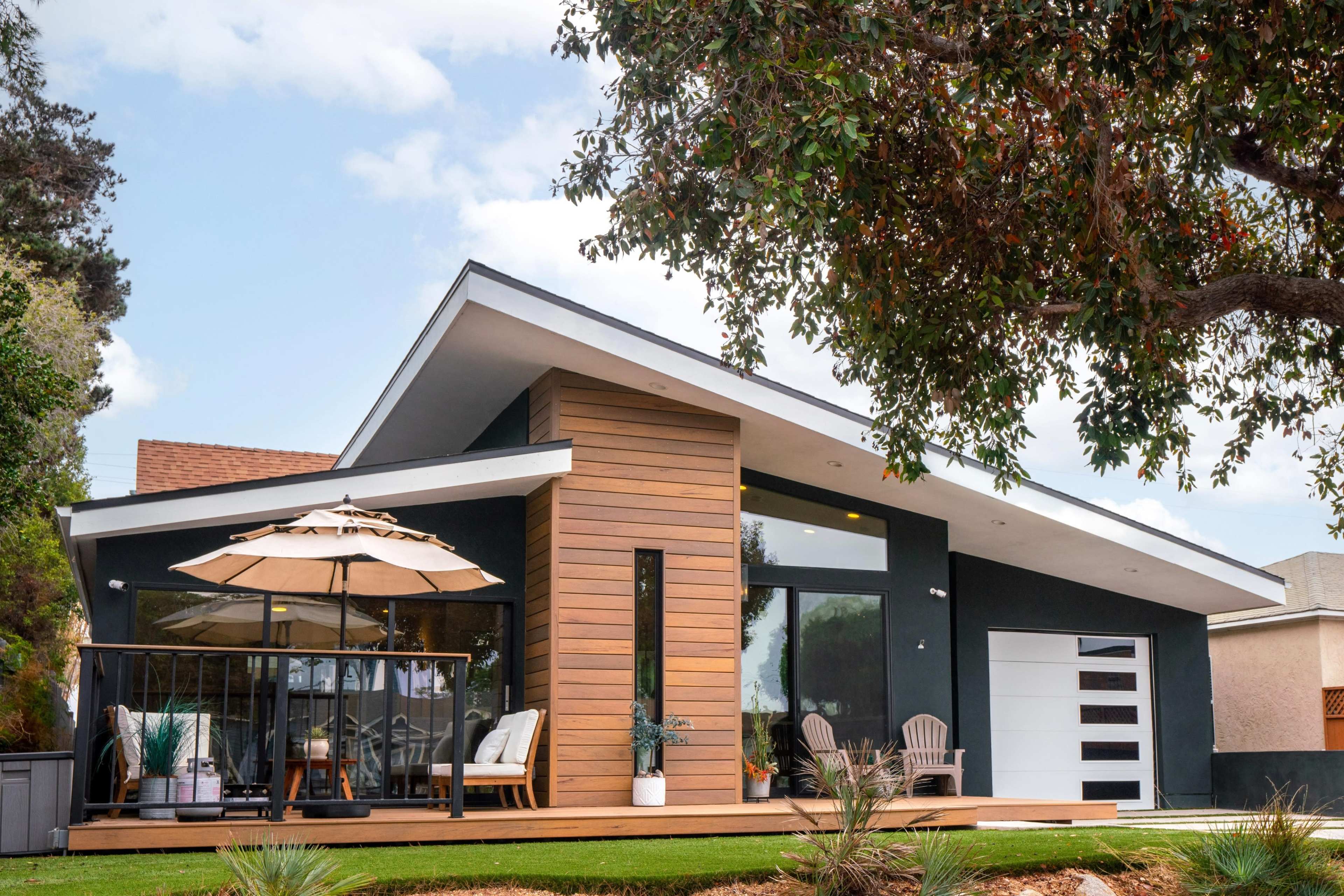 A modern home features a slanted roof, wooden accents, and a patio with an umbrella.
