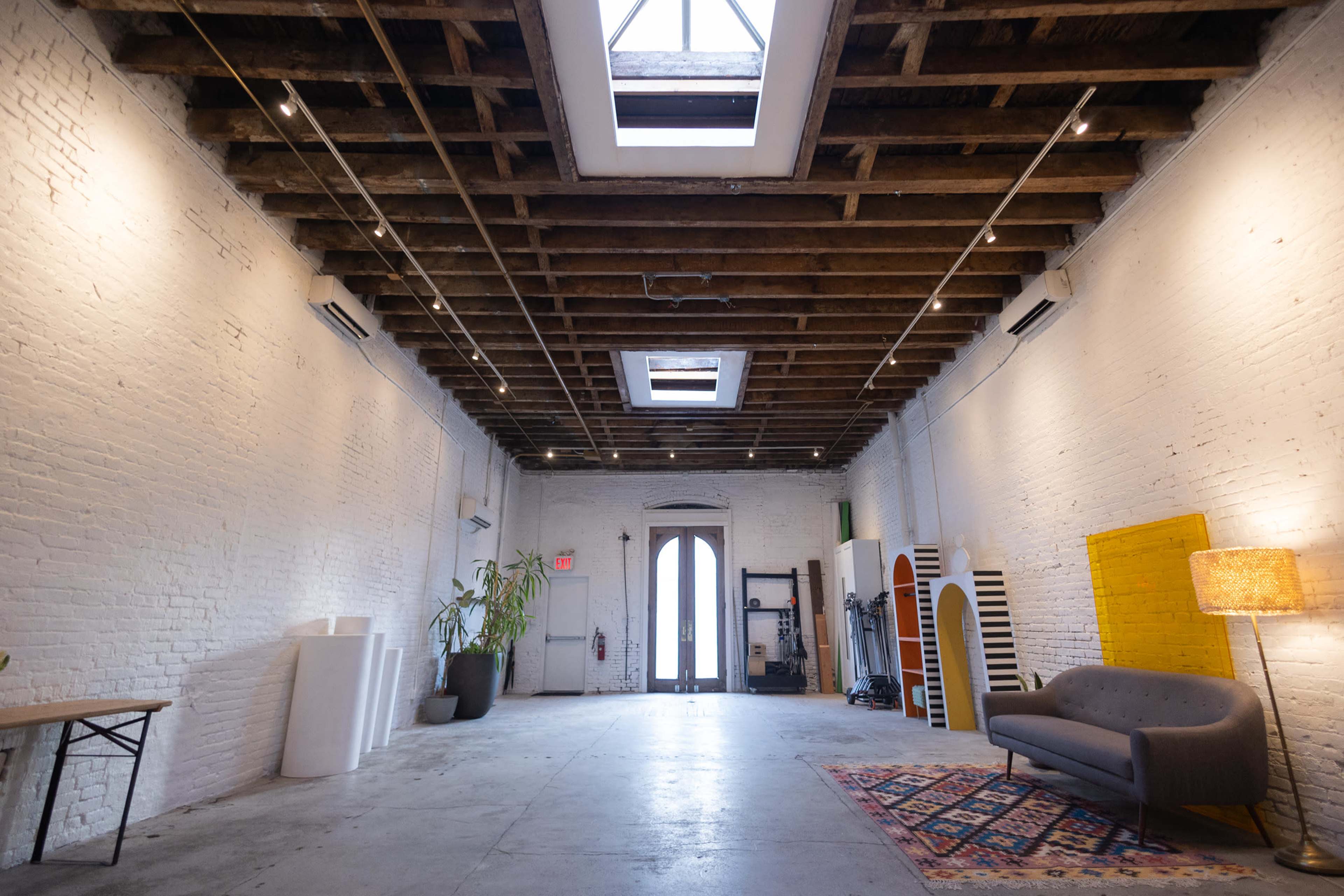 A spacious, well-lit loft interior with exposed brick walls, a wooden ceiling, and large windows letting in natural light.