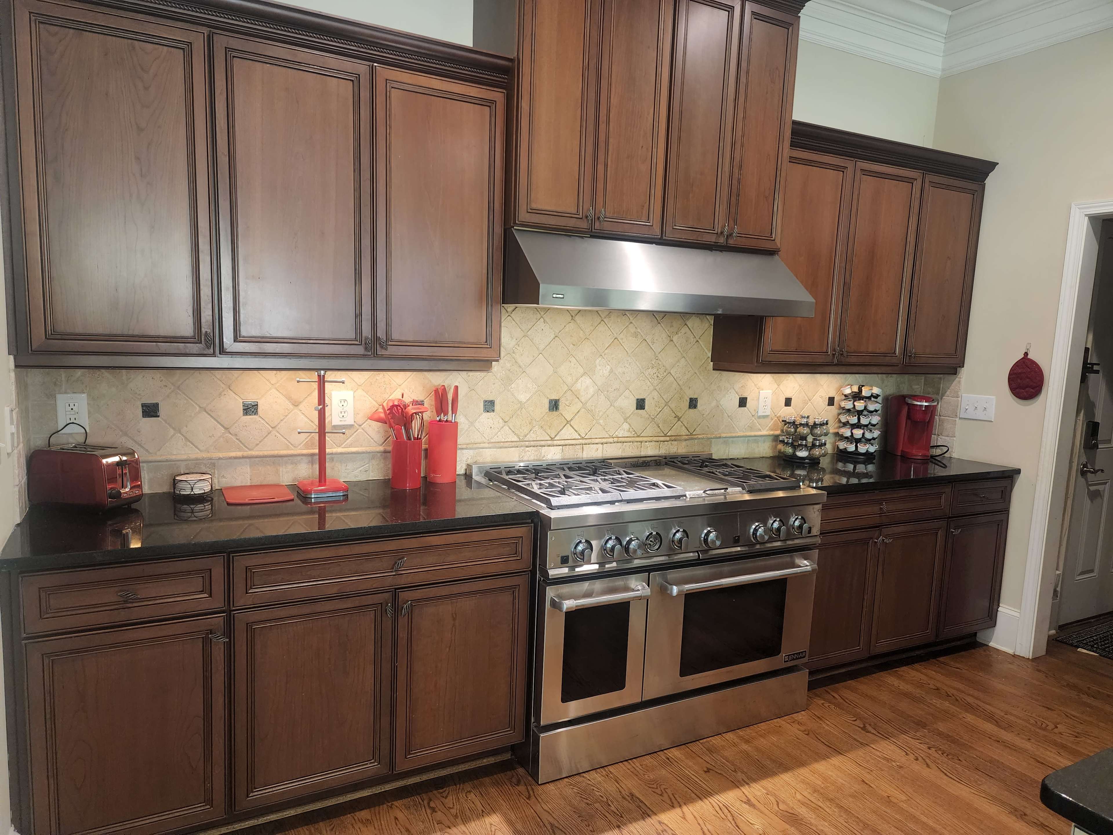 A spacious kitchen features dark wood cabinets, a stainless steel gas range, and a granite countertop with red and black accents.