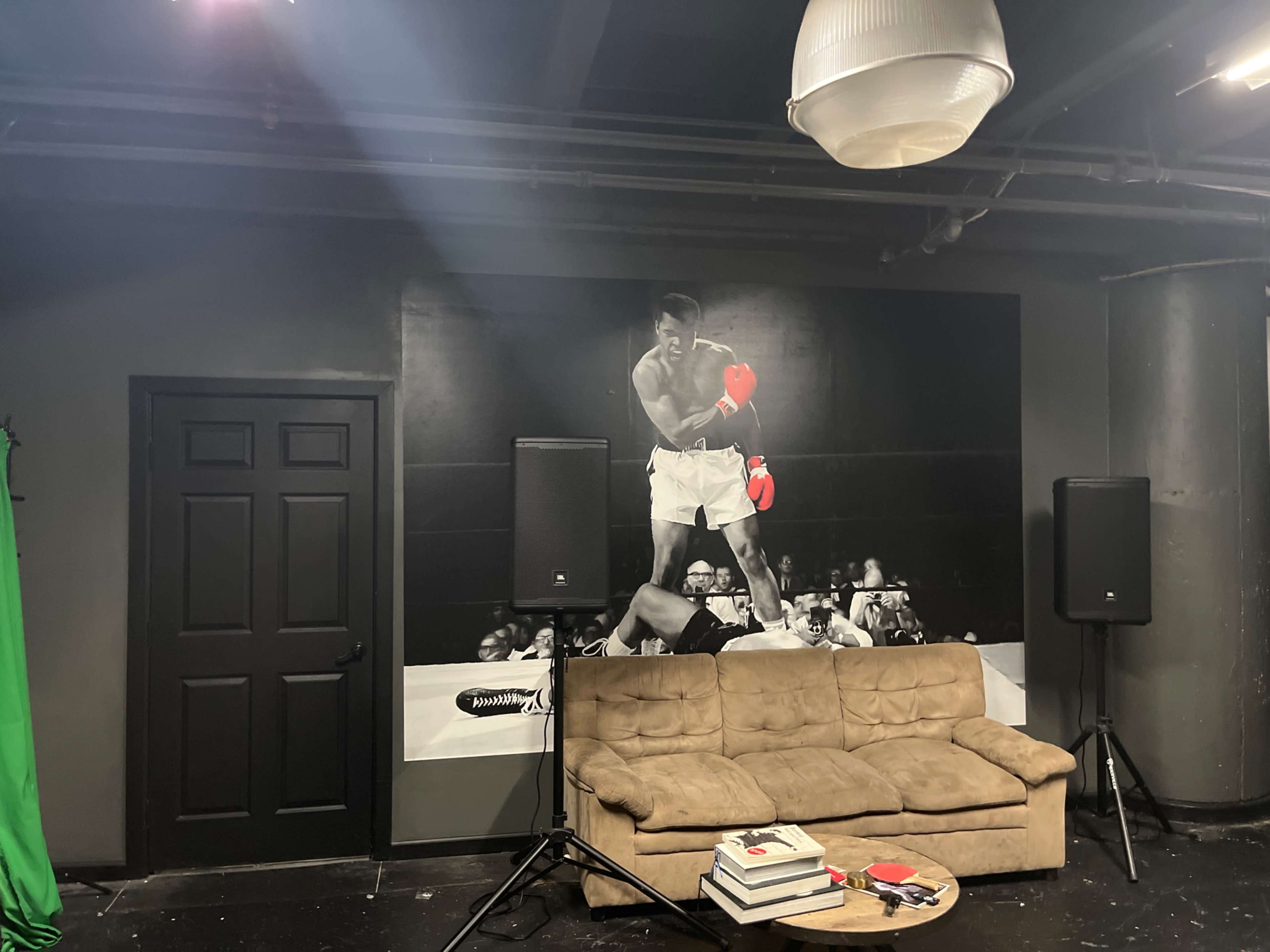 A boxing-themed studio space with a large black-and-white mural of a boxer on the wall behind a beige couch and speakers.