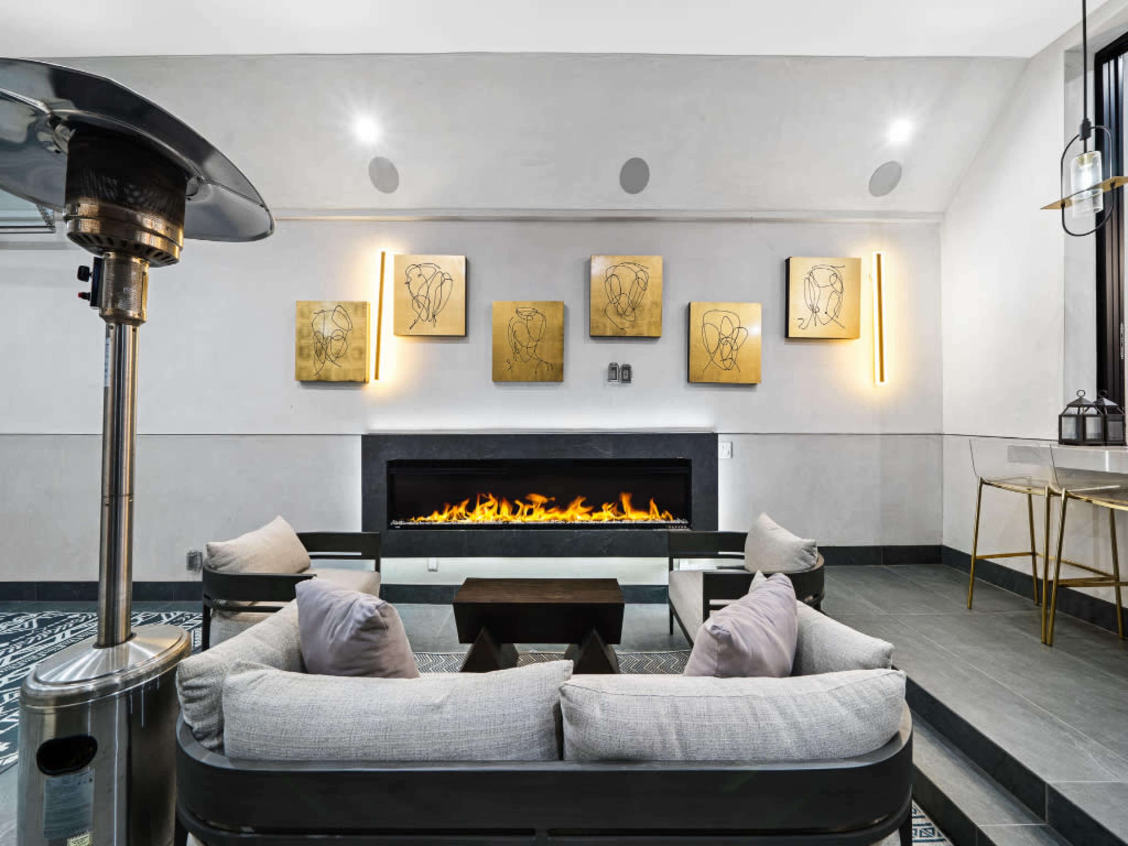 The image shows a modern living room with a linear fireplace, minimalist furniture, and abstract gold wall art.