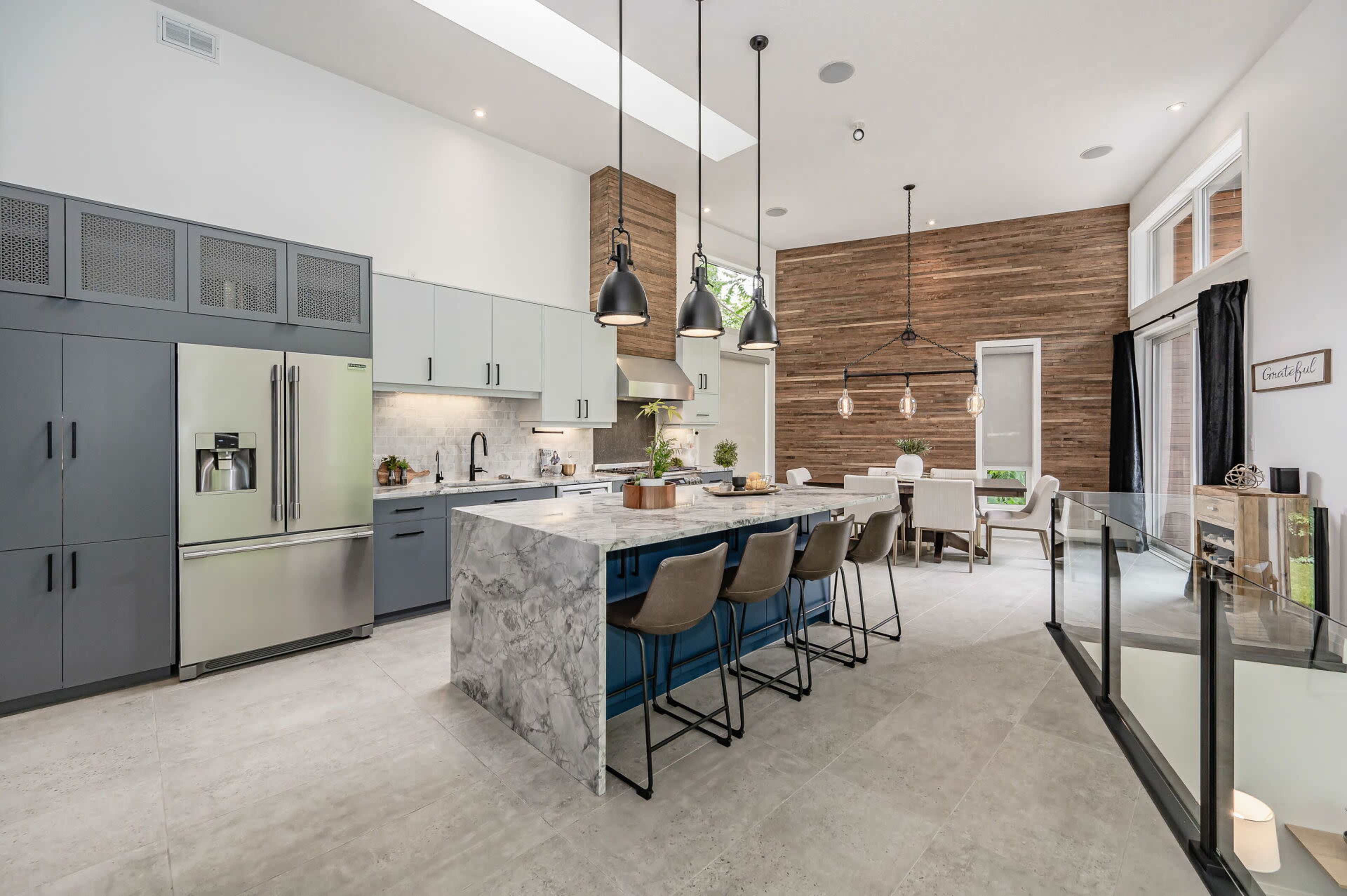 A modern kitchen with a central island, stainless steel appliances, and wooden accent walls, illuminated by pendant lighting.
