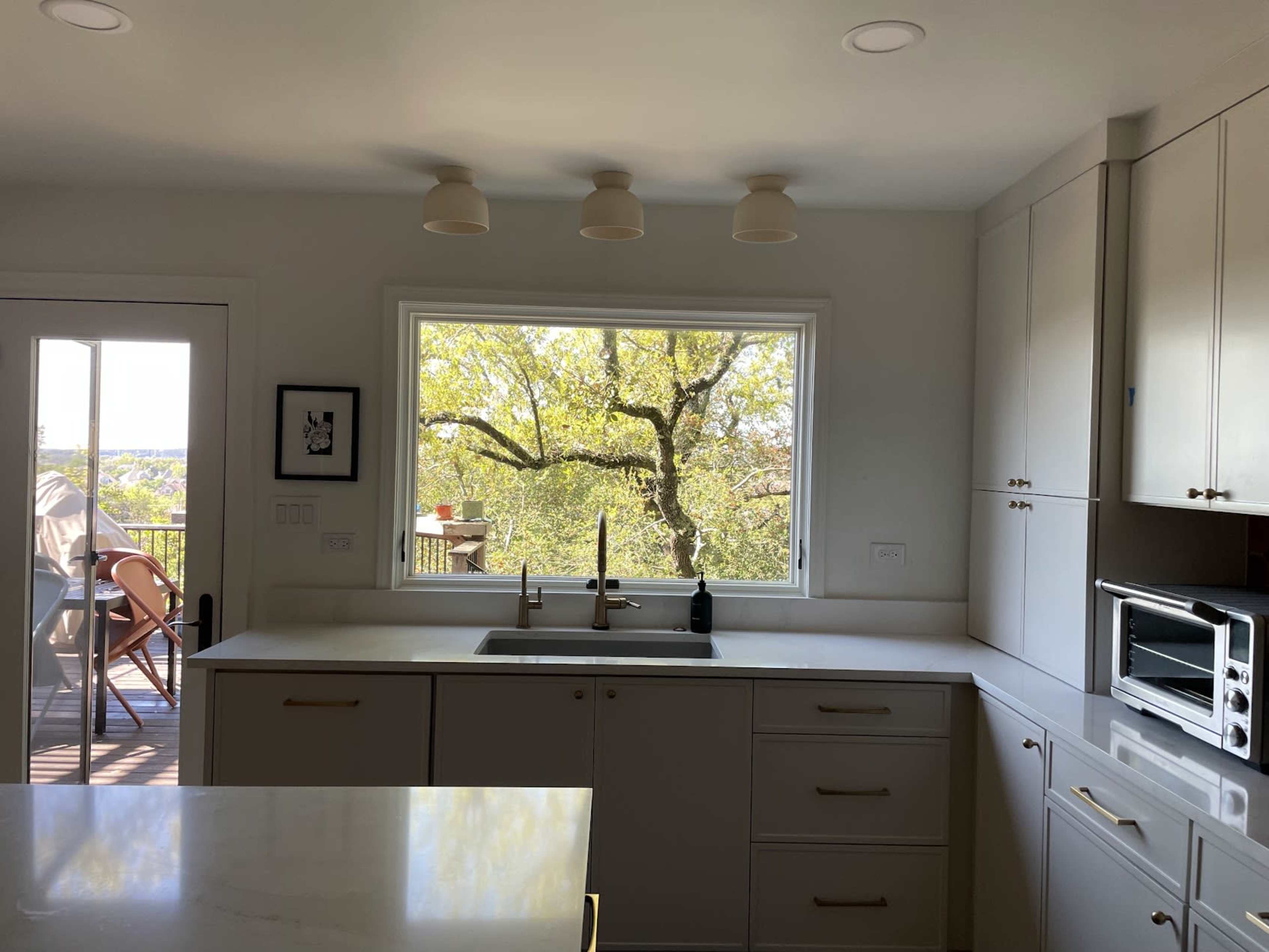 The image shows a modern kitchen with a large window overlooking a tree-filled outdoor area.
