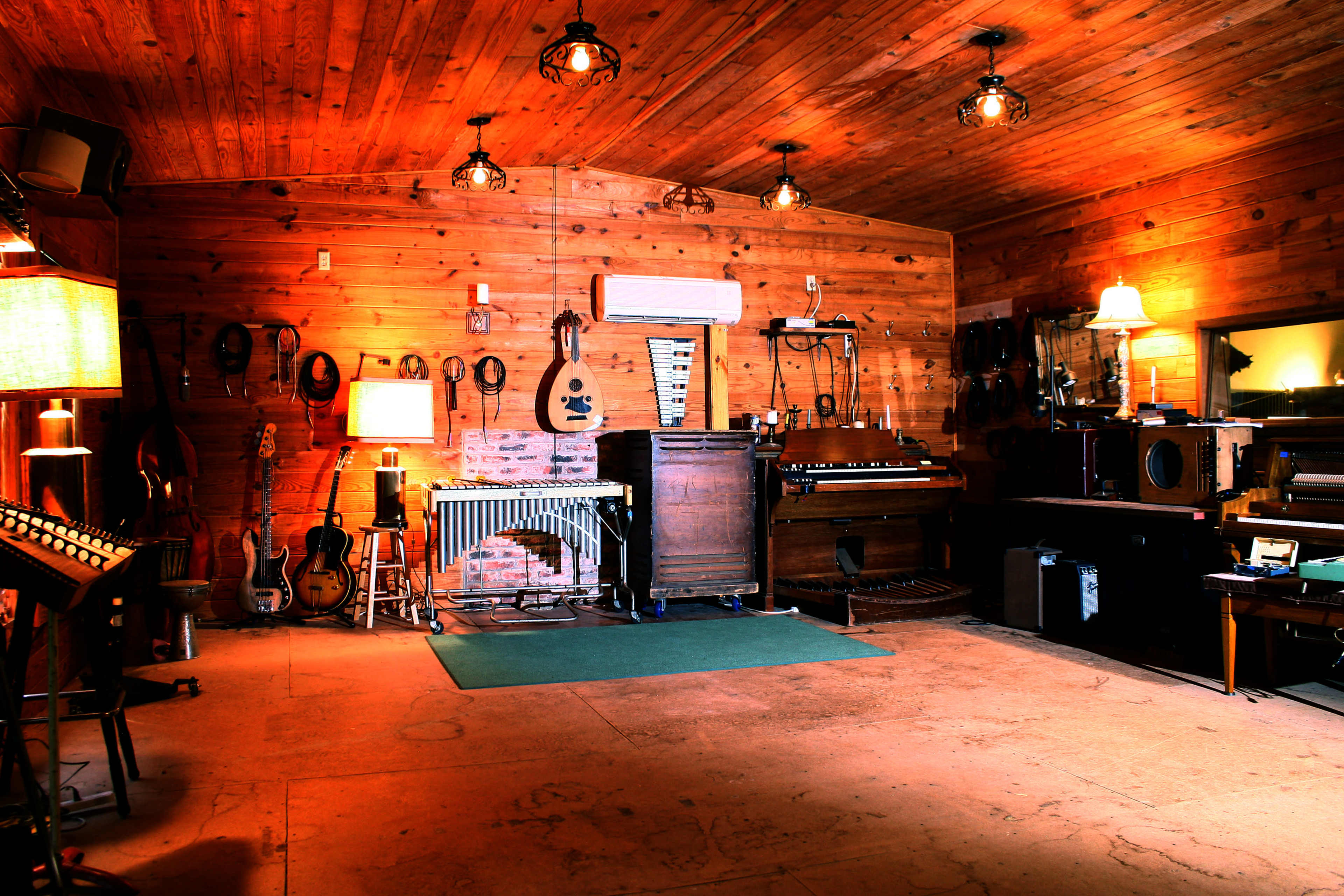 A wooden studio space filled with various musical instruments, including guitars and an upright piano, under warm lighting.