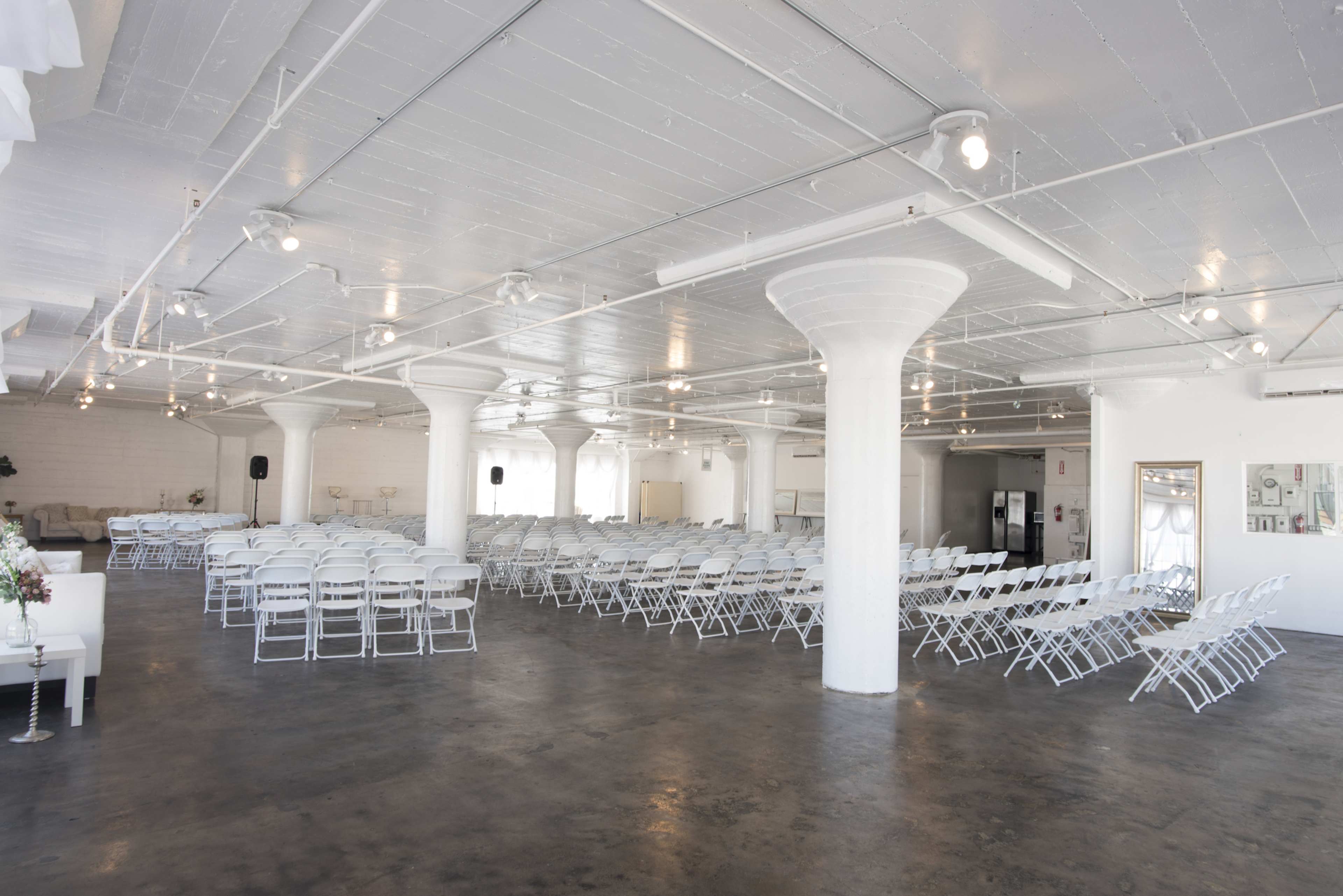 A spacious, modern venue arranged with rows of white folding chairs and featuring white columns and bright lighting.