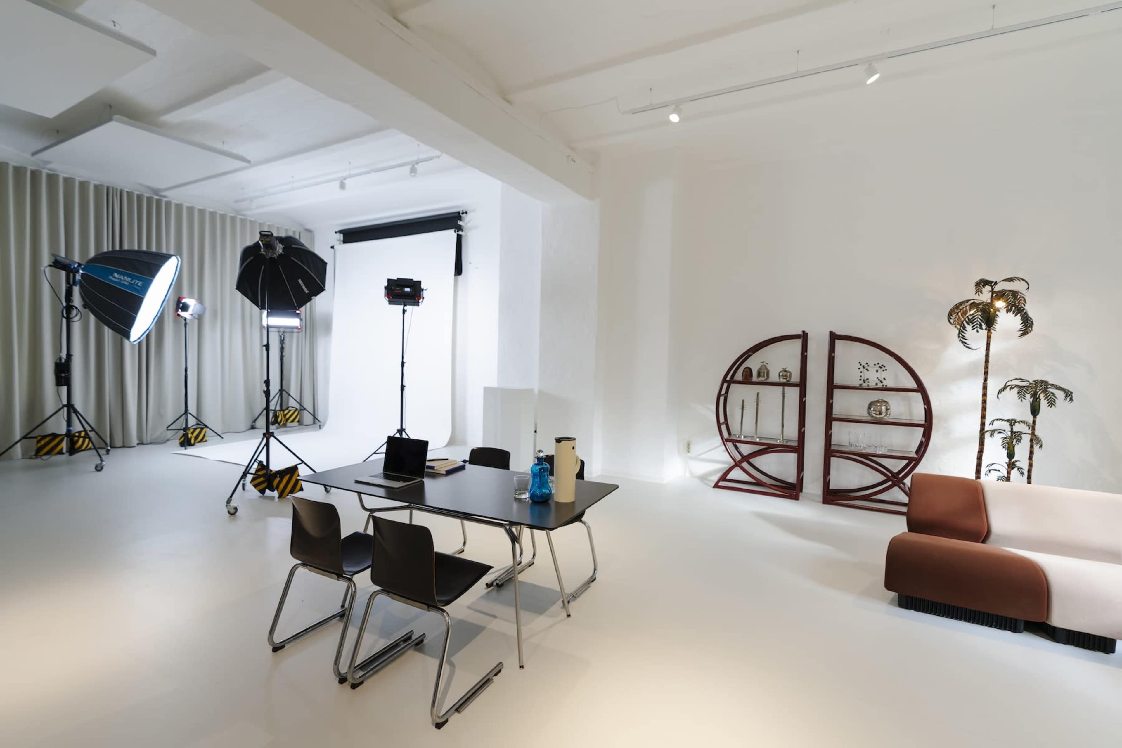 A spacious, well-lit studio features a table with chairs, photography equipment, and decorative elements including a unique bookshelf and a plant.
