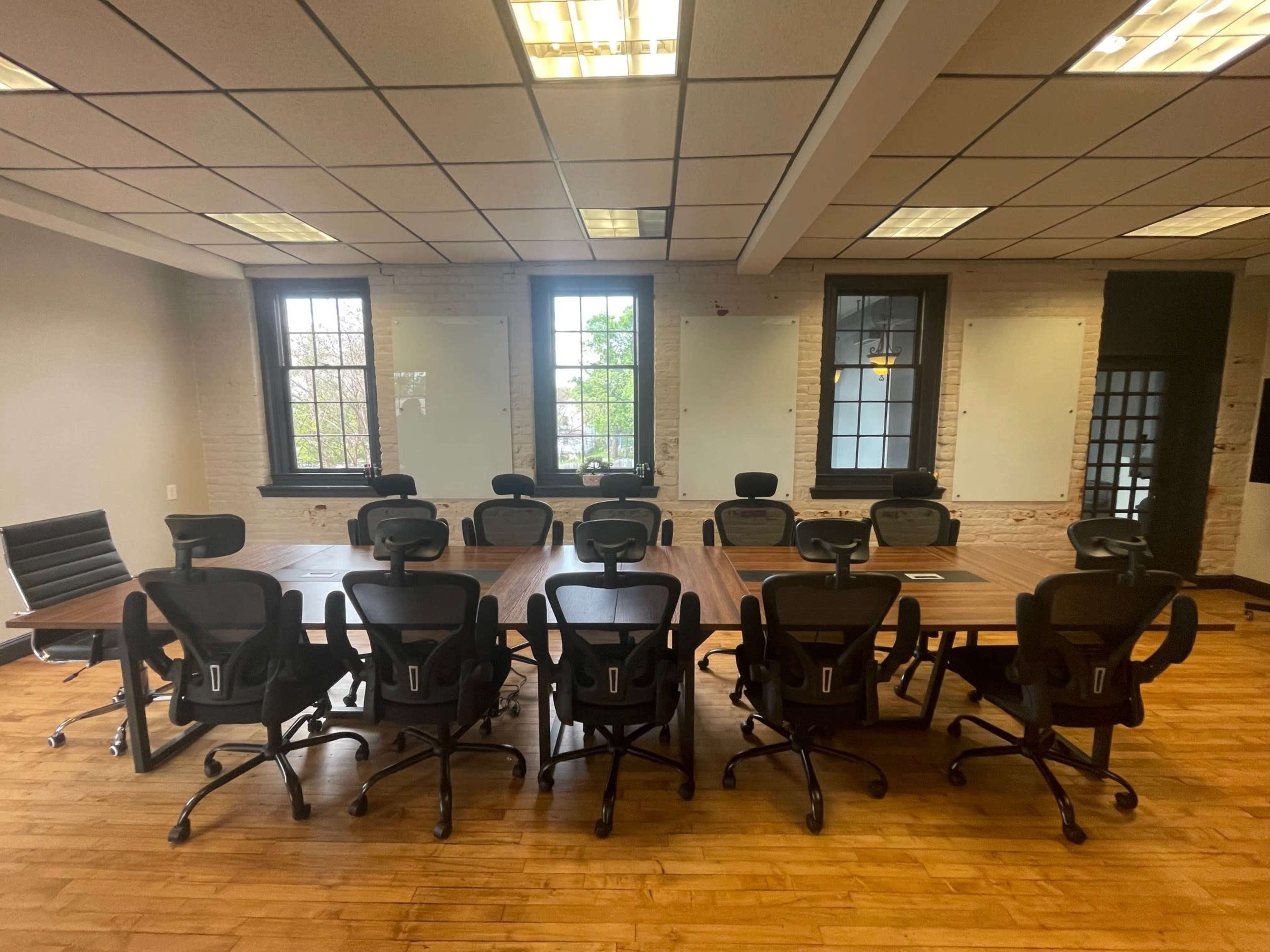 A large conference room features a long wooden table surrounded by black ergonomic chairs, with windows providing natural light.