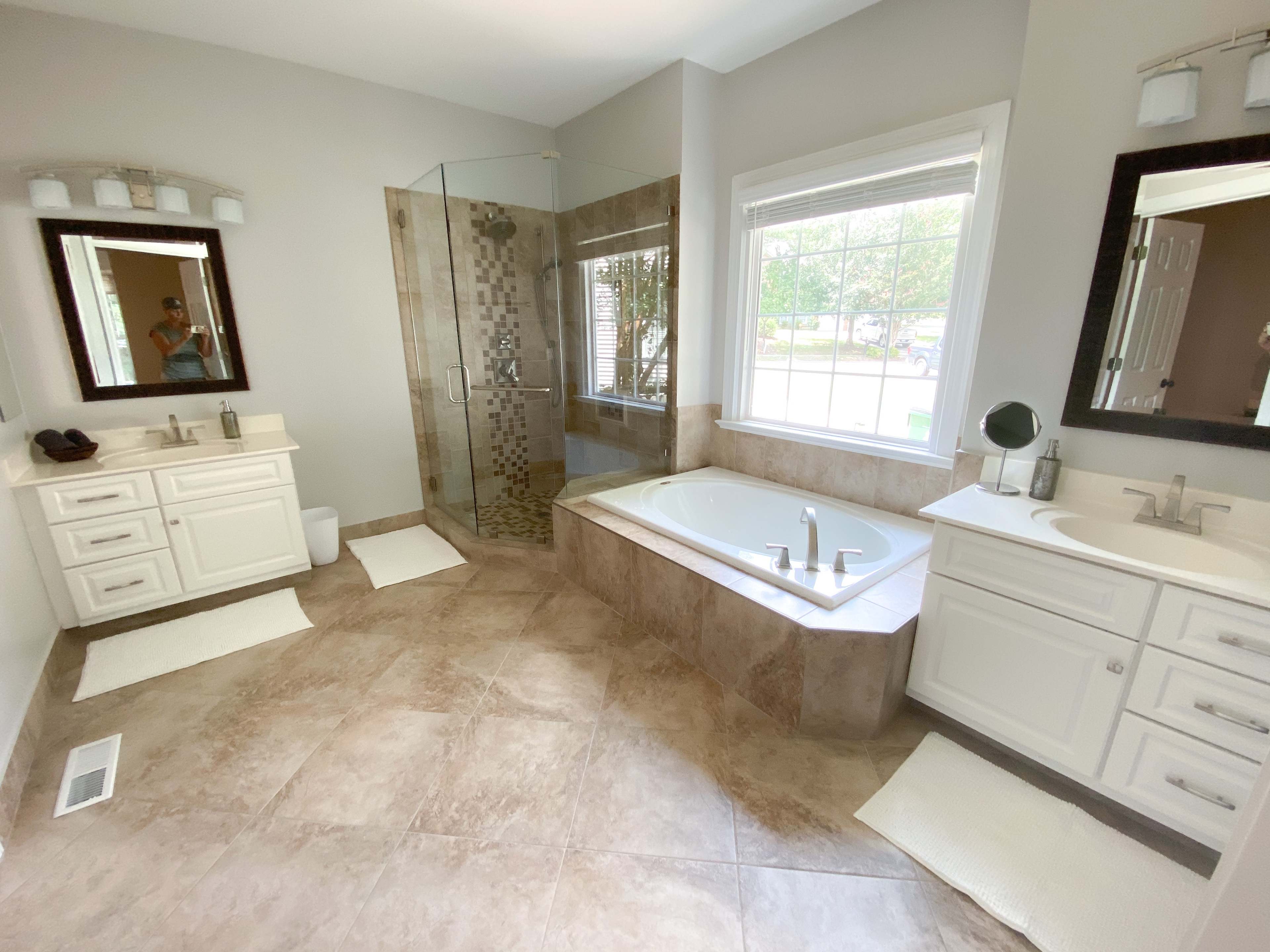 A spacious bathroom features a glass shower, a large tub, double sinks, and natural light from a window.