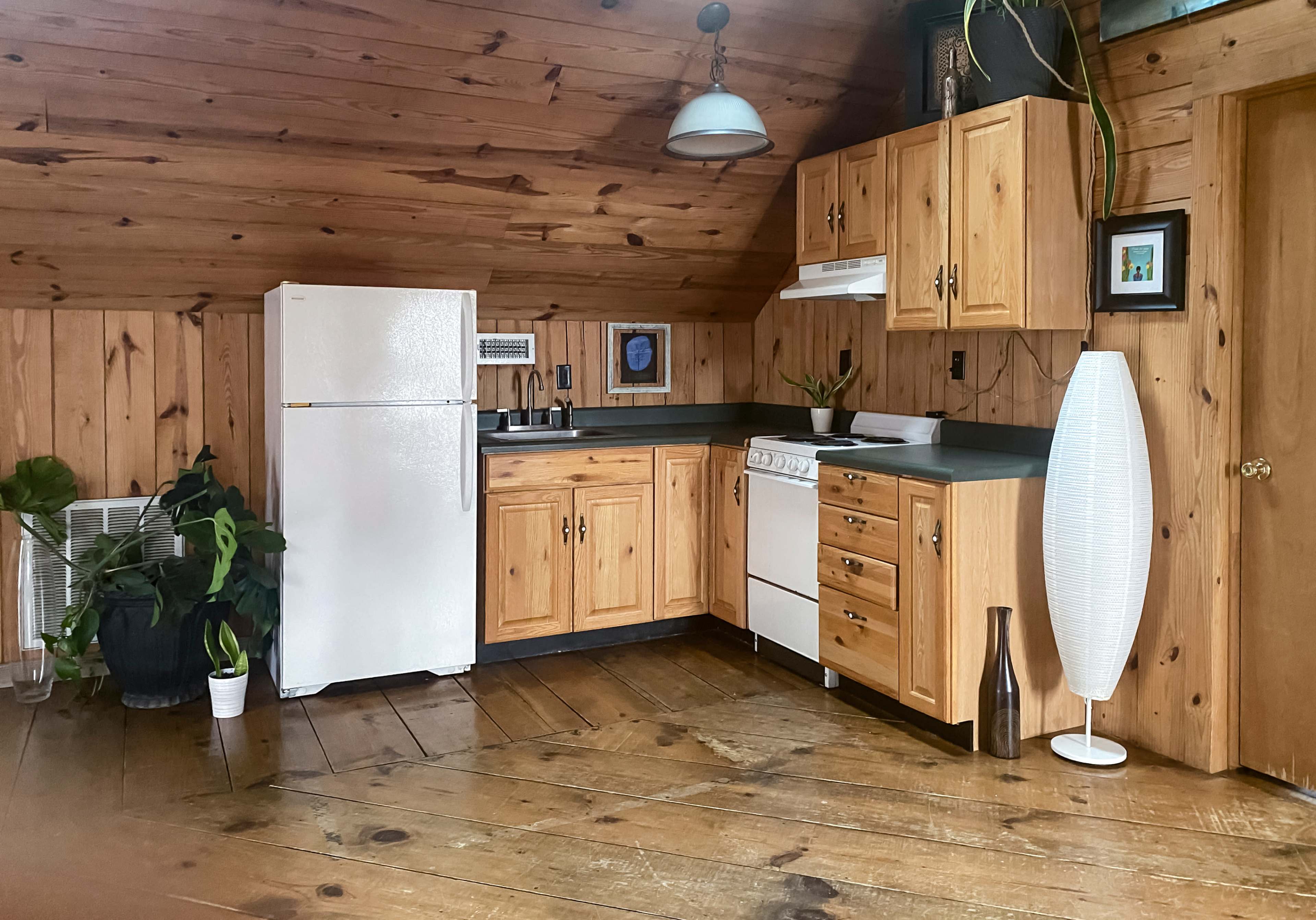 The kitchen features wooden walls and floors, with a white refrigerator, stove, and cabinetry arranged in a functional layout.