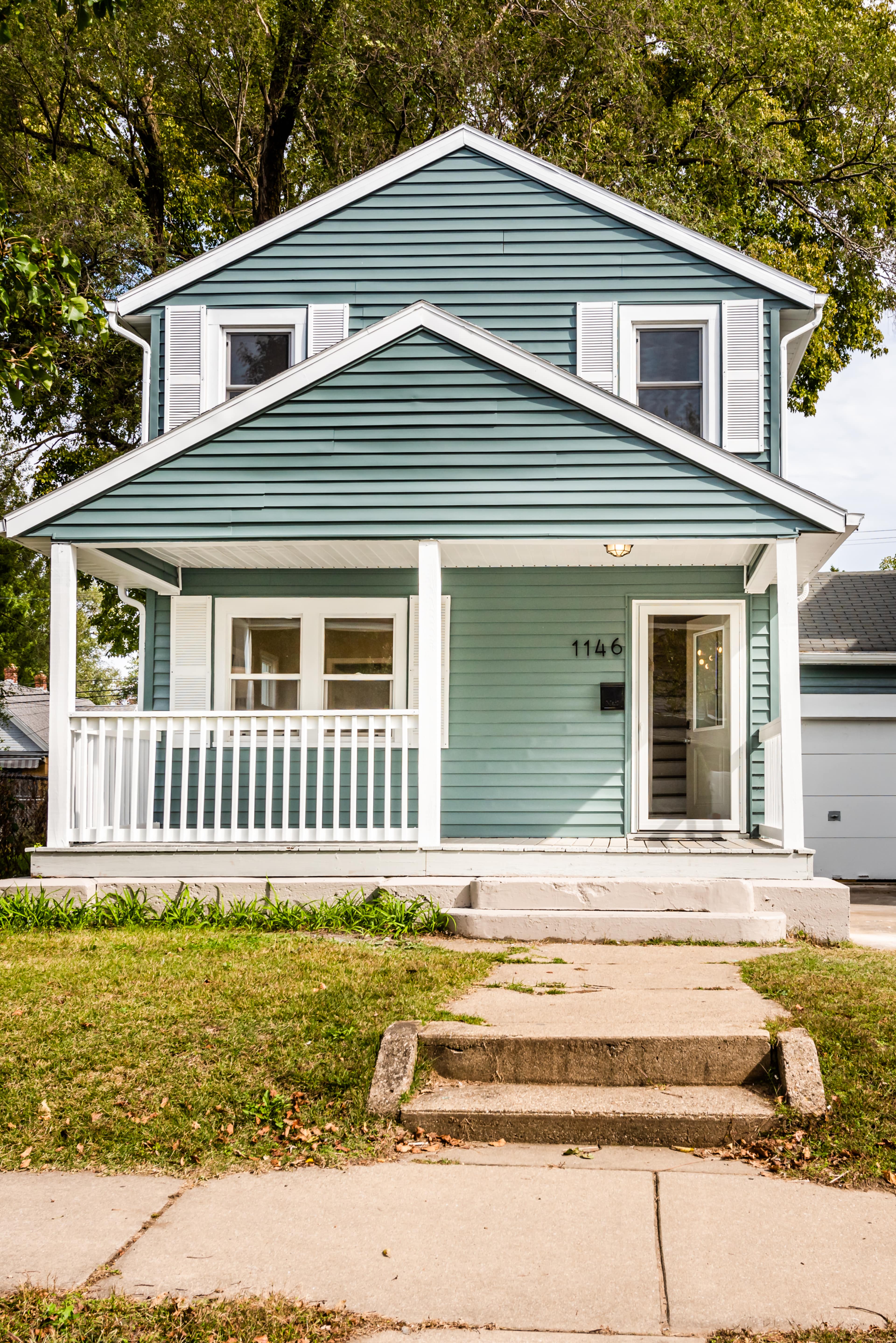 A light blue two-story house with white trim, a front porch, and a walkway leading up to it.