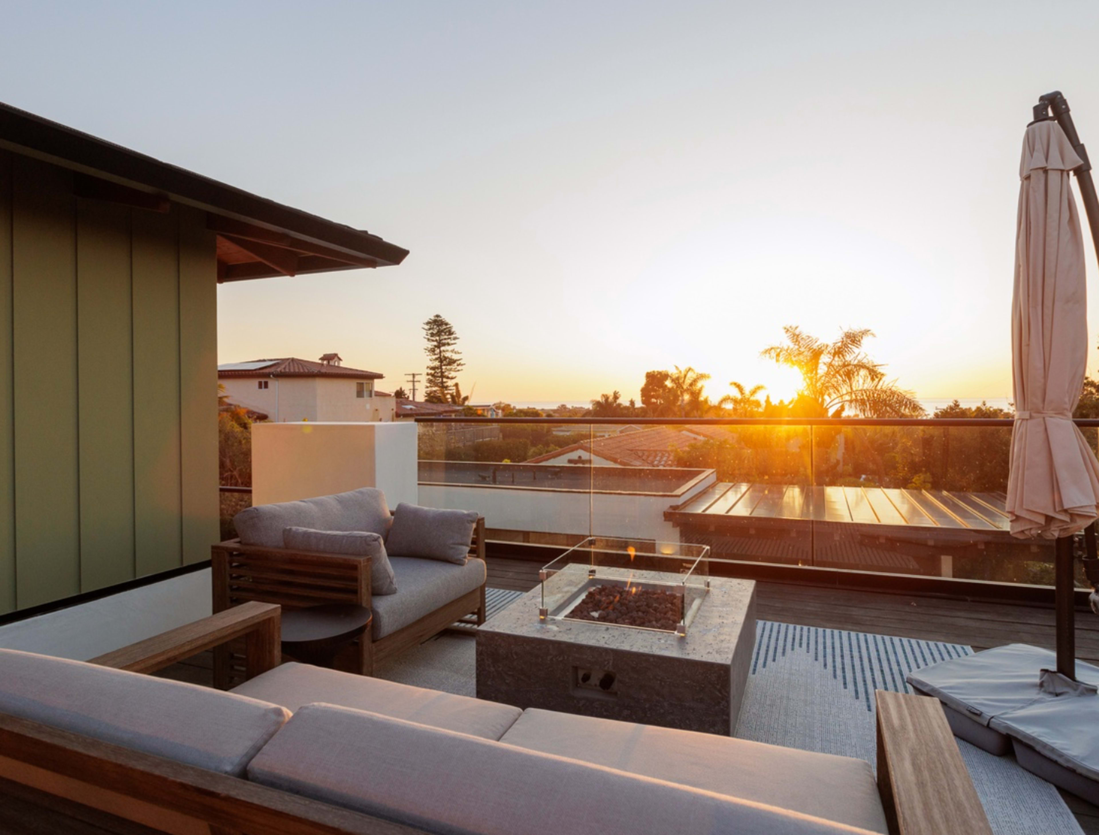 A rooftop terrace features a cozy seating area with a fire pit, and the sun sets in the background.