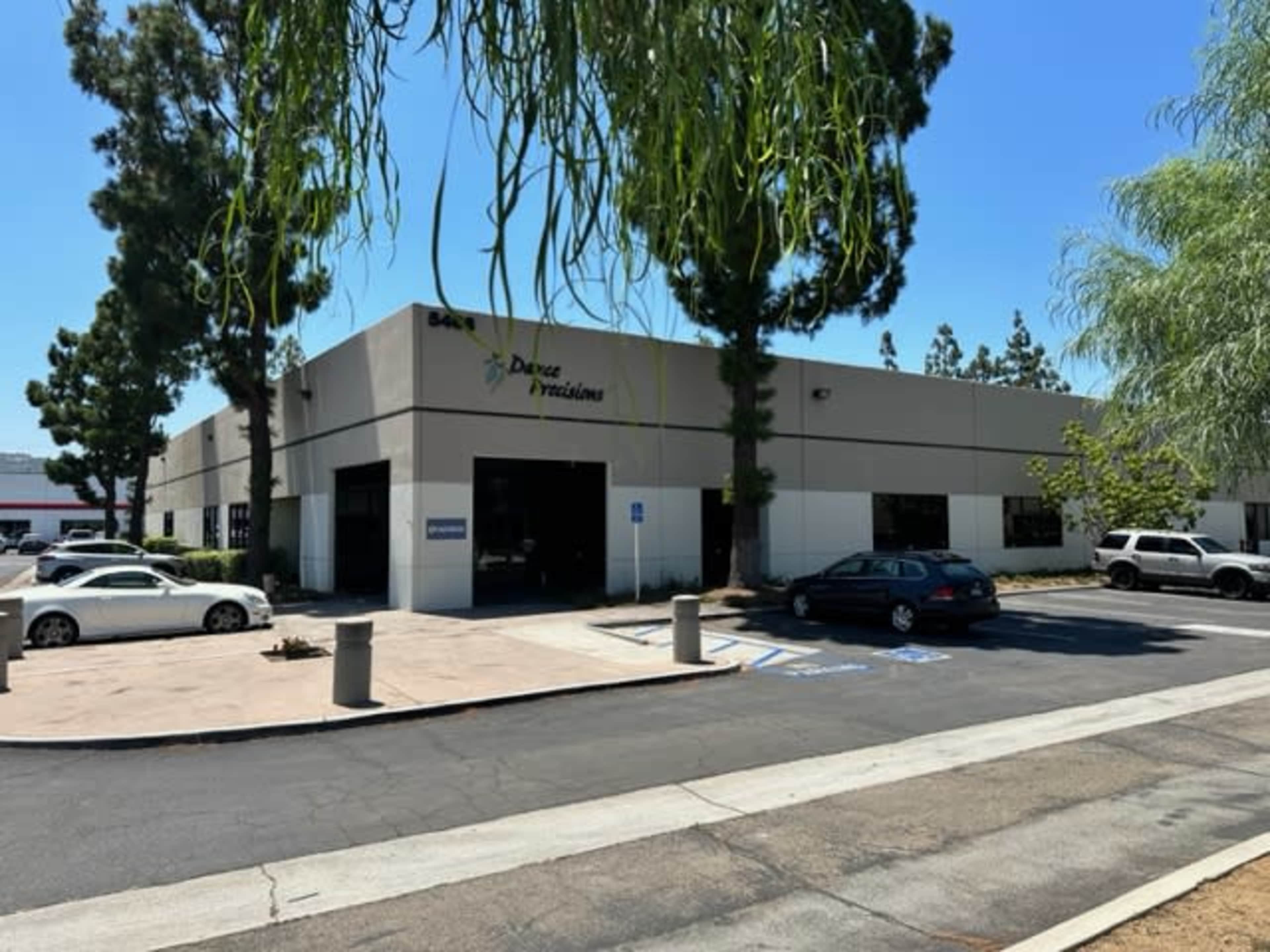 A single-story commercial building with parking spaces and trees in front, labeled "Dance Precisions."