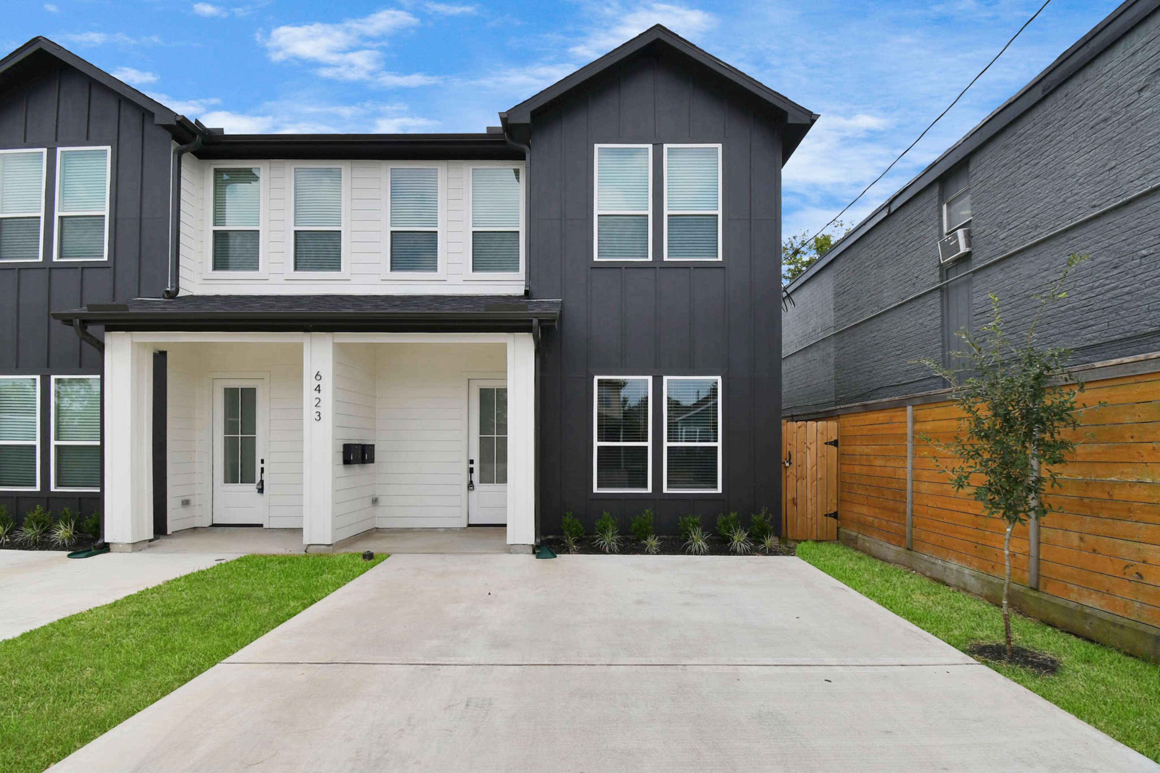 A modern duplex with a dark exterior and two entrances, surrounded by a landscaped yard and a driveway.