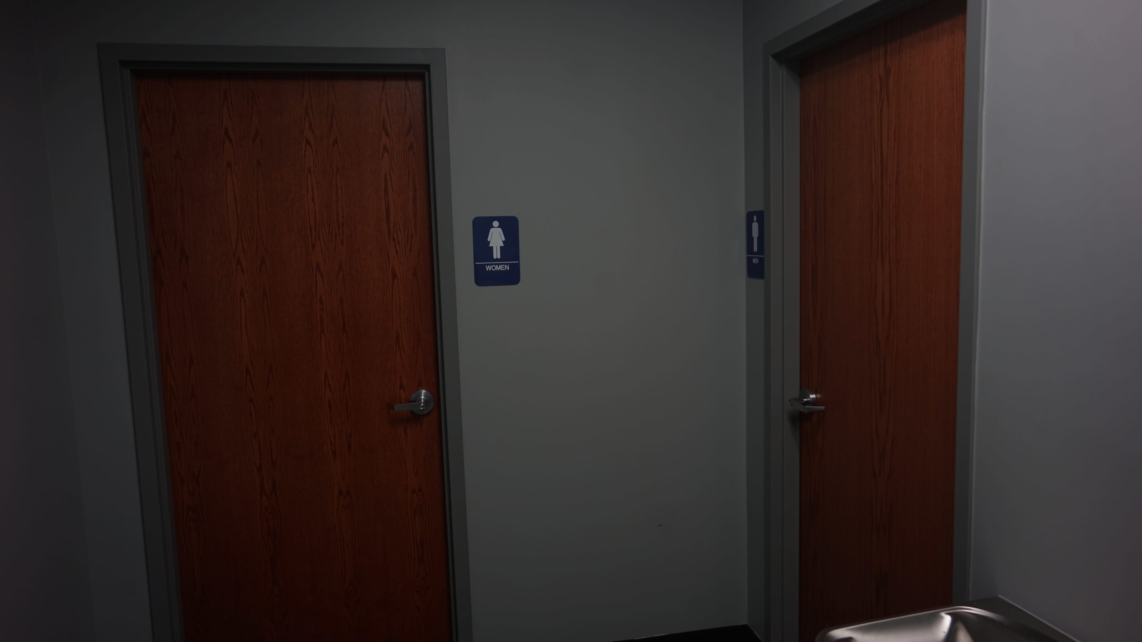 Two closed wooden restroom doors in a corridor, one marked for women's use.