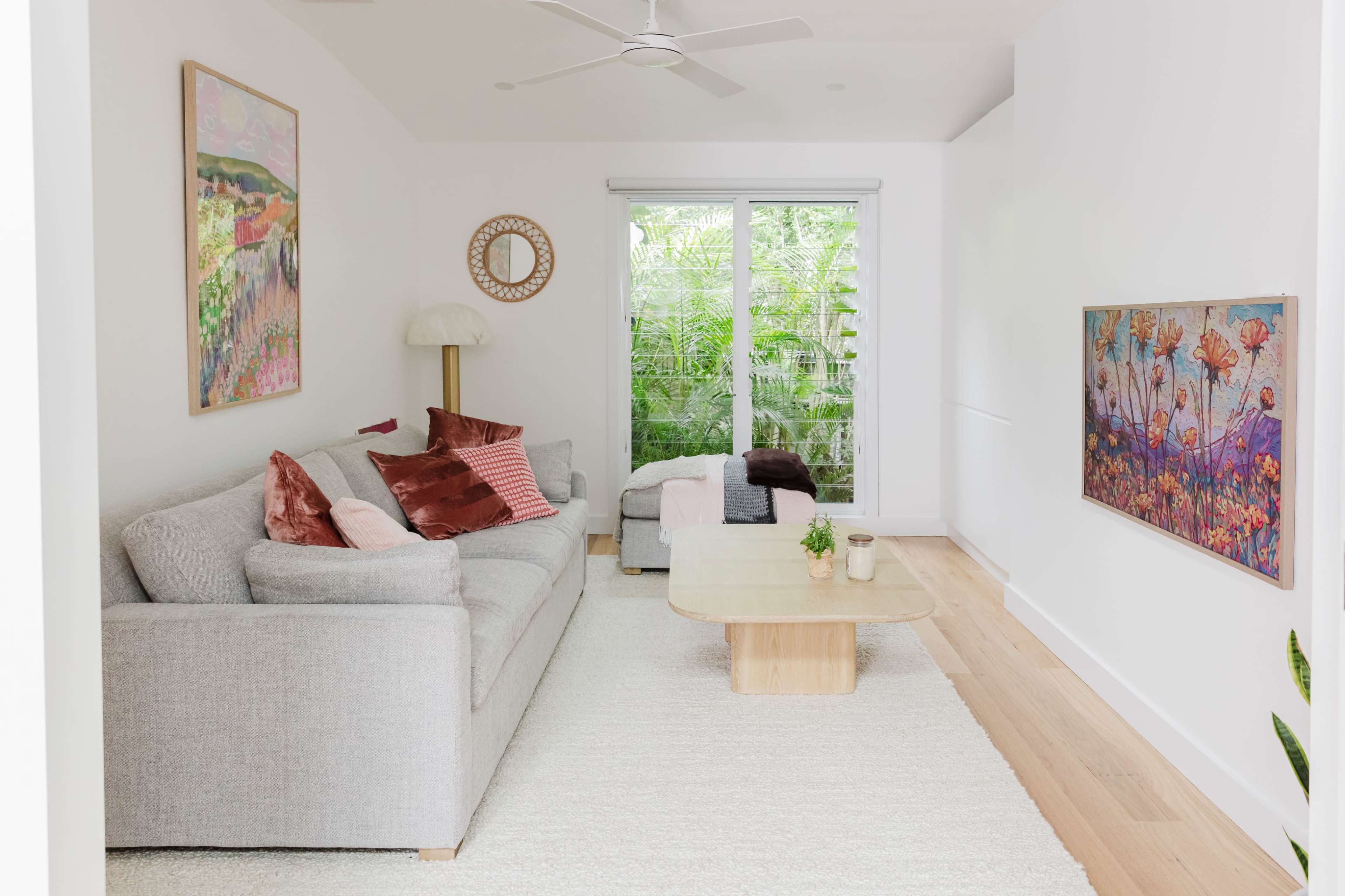 The image shows a modern living room with a gray sofa, a wooden coffee table, and large windows overlooking a green outdoor area.