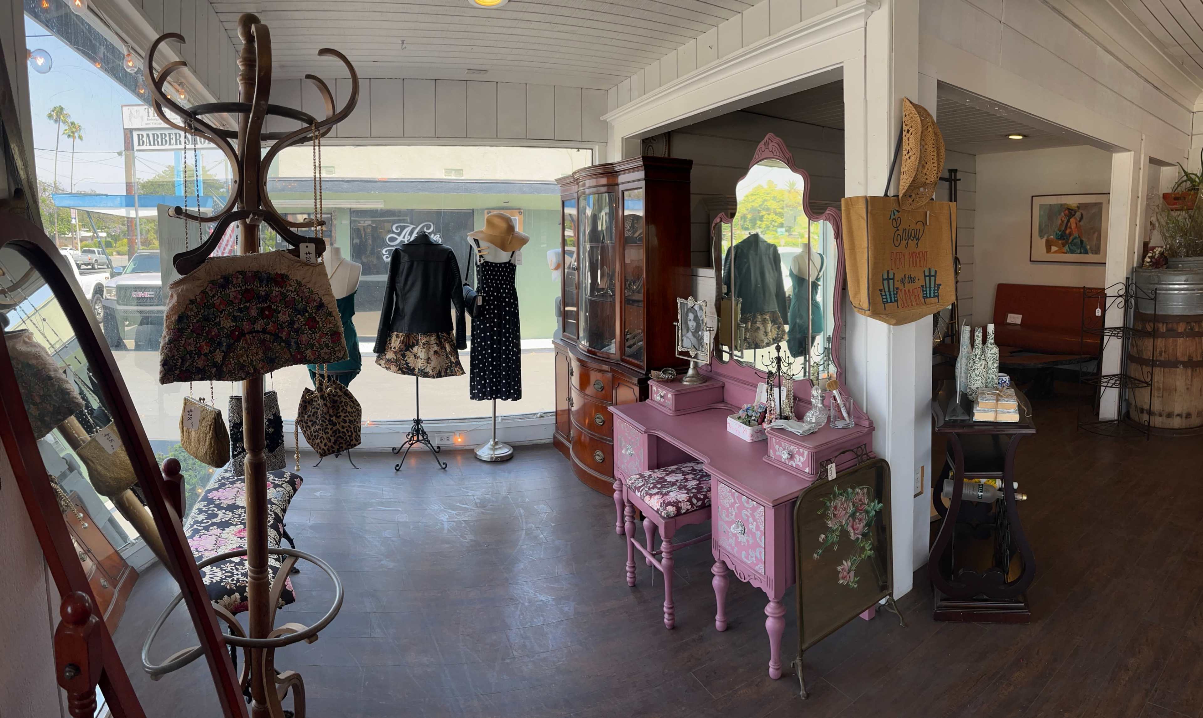 The image shows a boutique interior featuring vintage clothing displays, a pink vanity, and various decorative items, all arranged in a well-lit space.