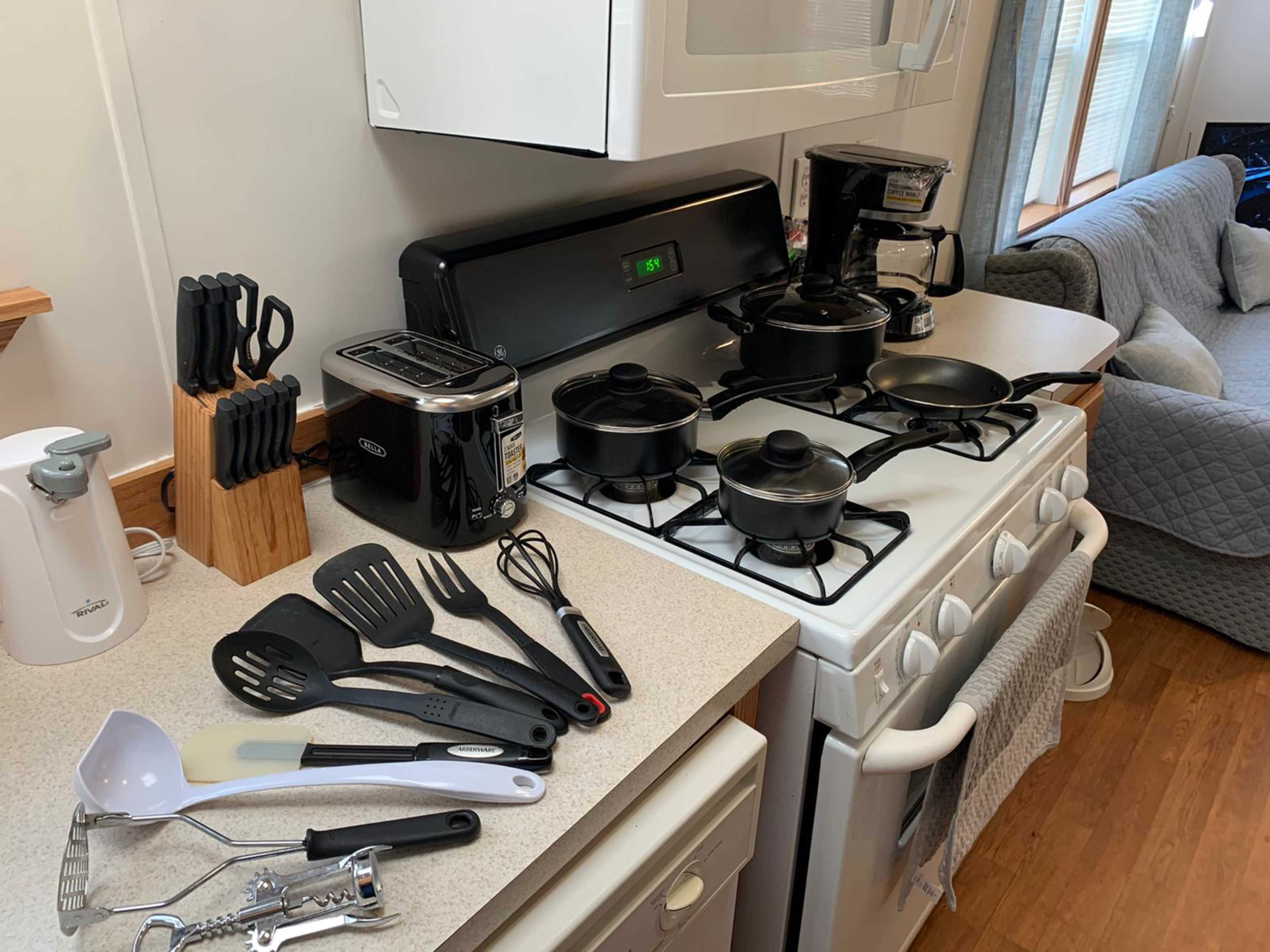 A kitchen counter features a stove with several black pots, utensils, and appliances, including a toaster and coffee maker.