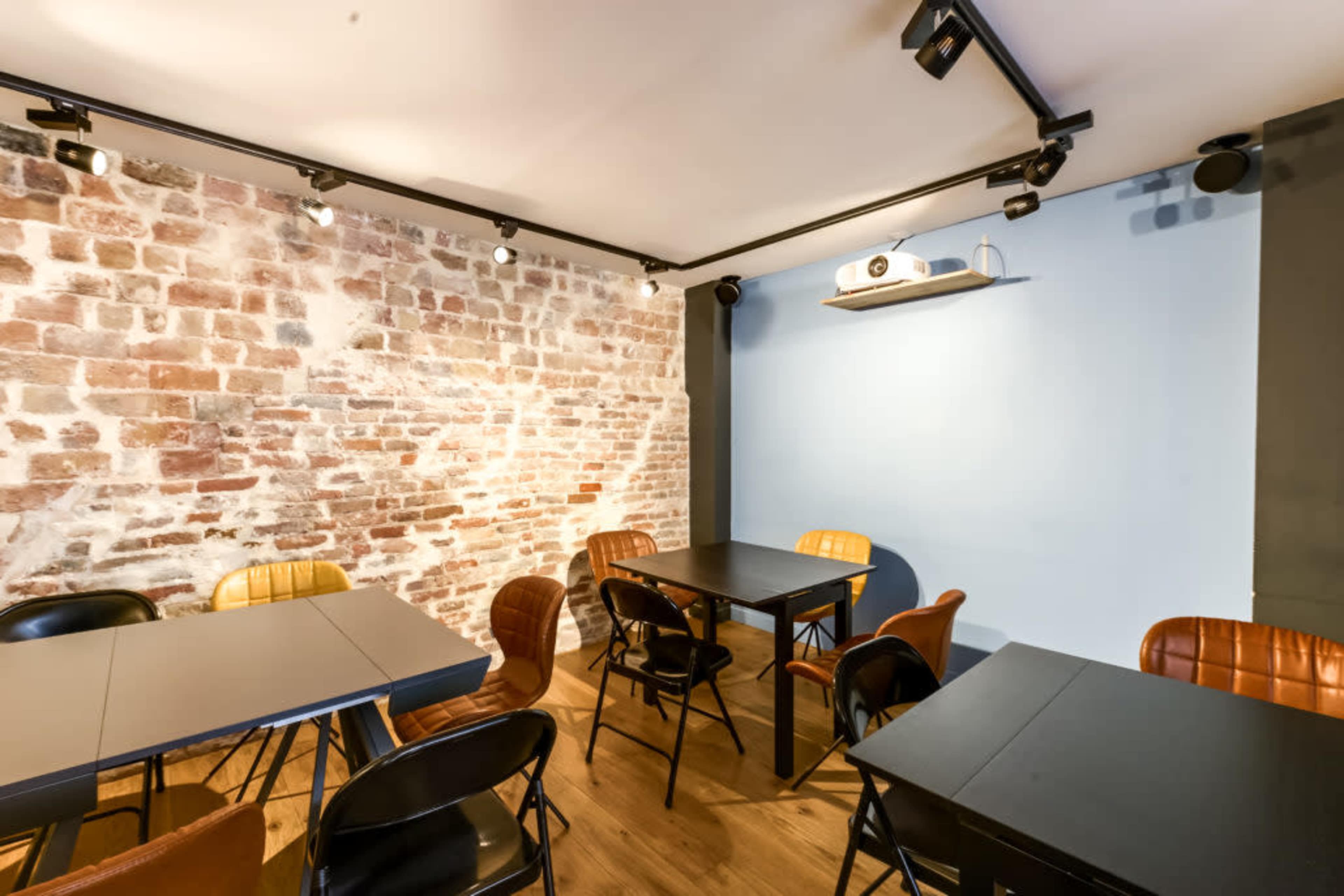 The image shows a dining area with several black tables and various chairs against a backdrop of a brick wall and a blue accent wall.