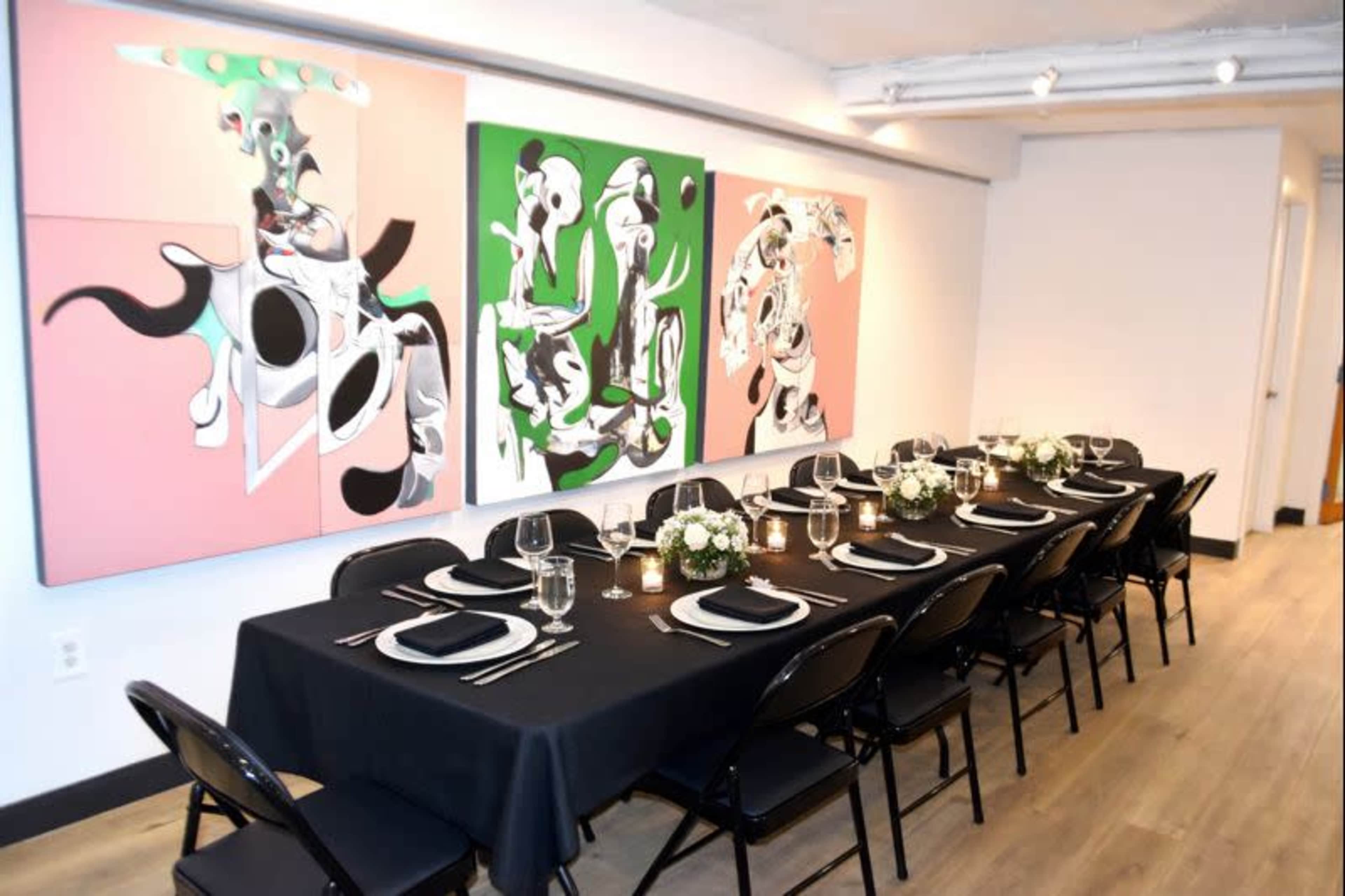 A long dining table with black linens is set for a meal in a room adorned with abstract artwork on the walls.