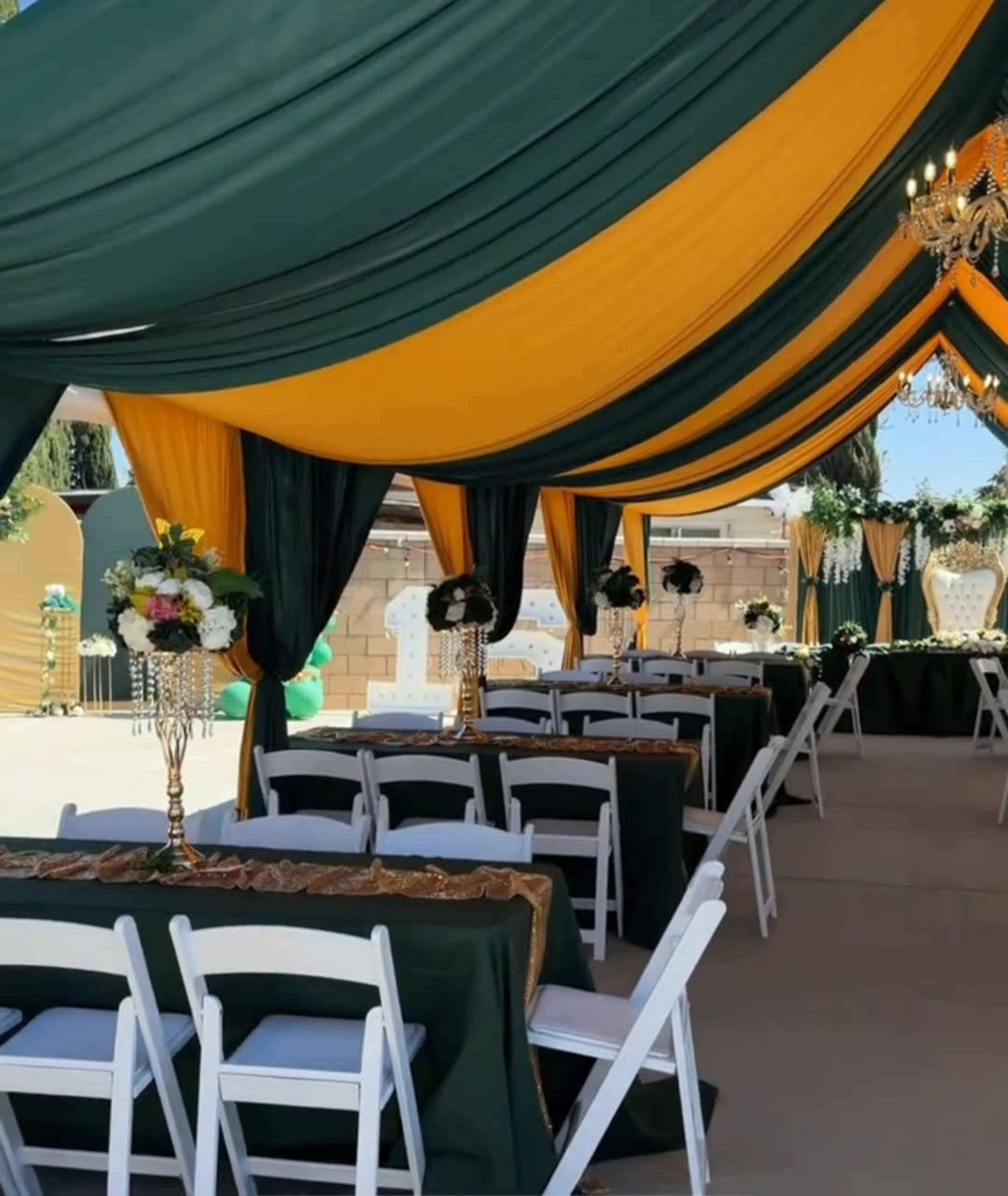 The image shows a beautifully decorated event tent featuring dark green and yellow drapery, with tables set for a formal gathering.