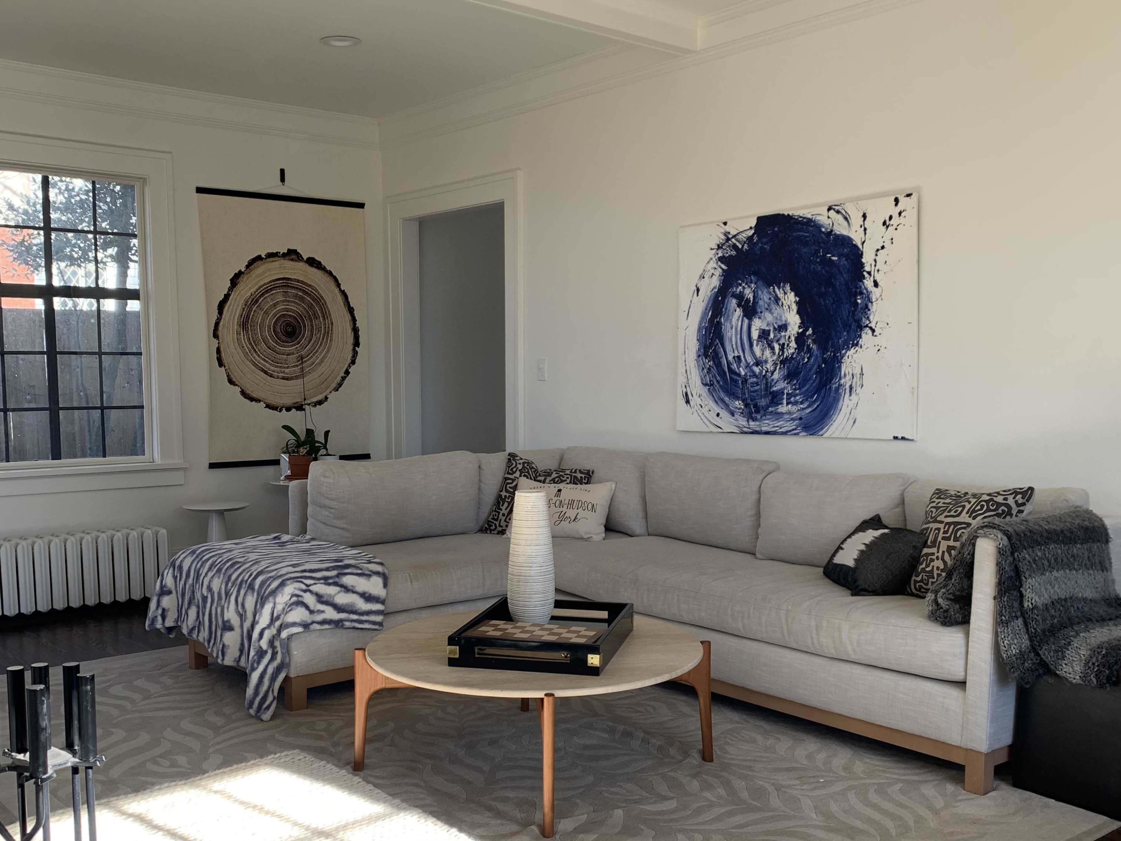 A modern living room with a large sectional sofa, a coffee table, and two pieces of art hanging on the walls.