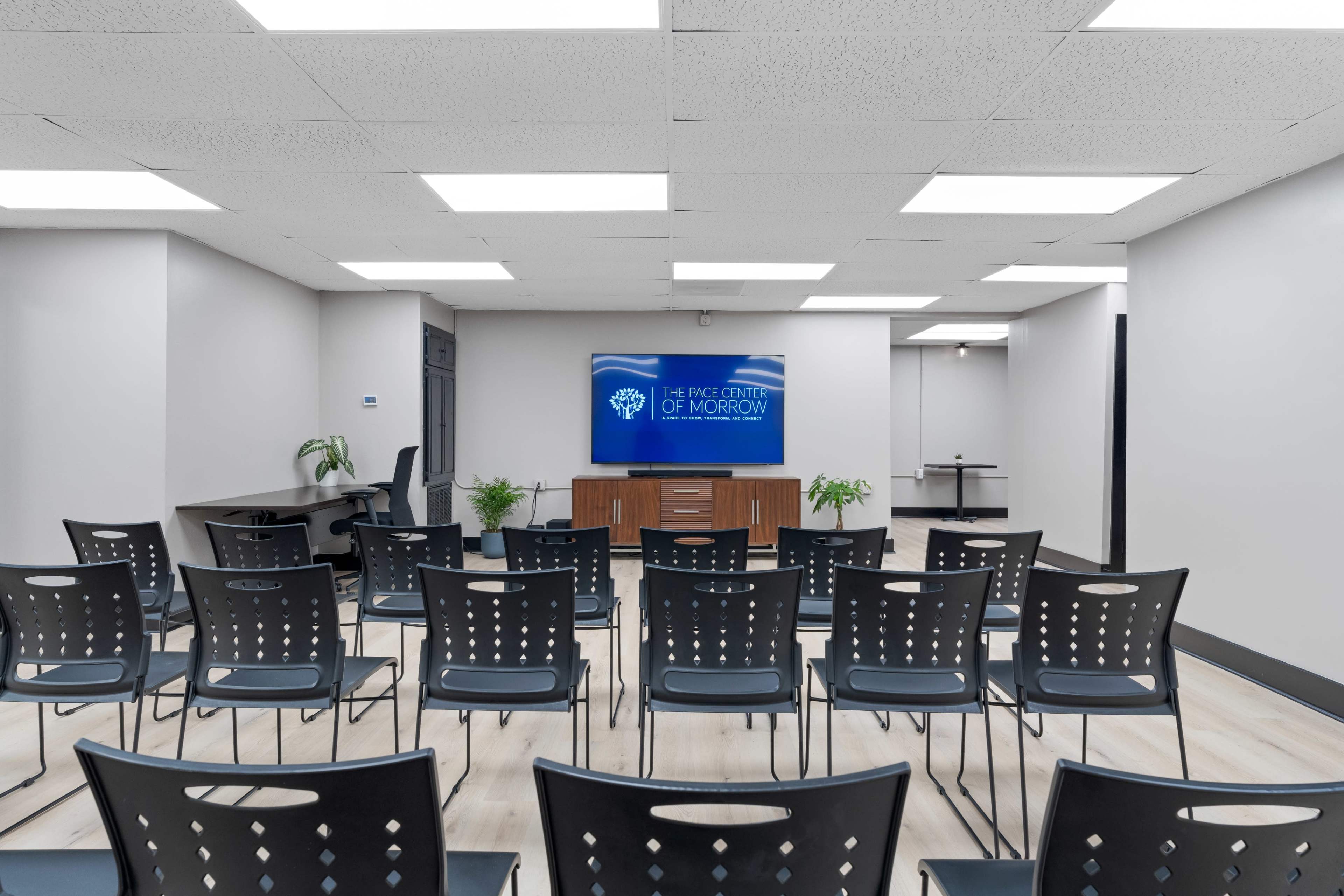 A conference room with rows of black chairs facing a wall-mounted display screen that reads "THE PACE CENTER OF MORROW."