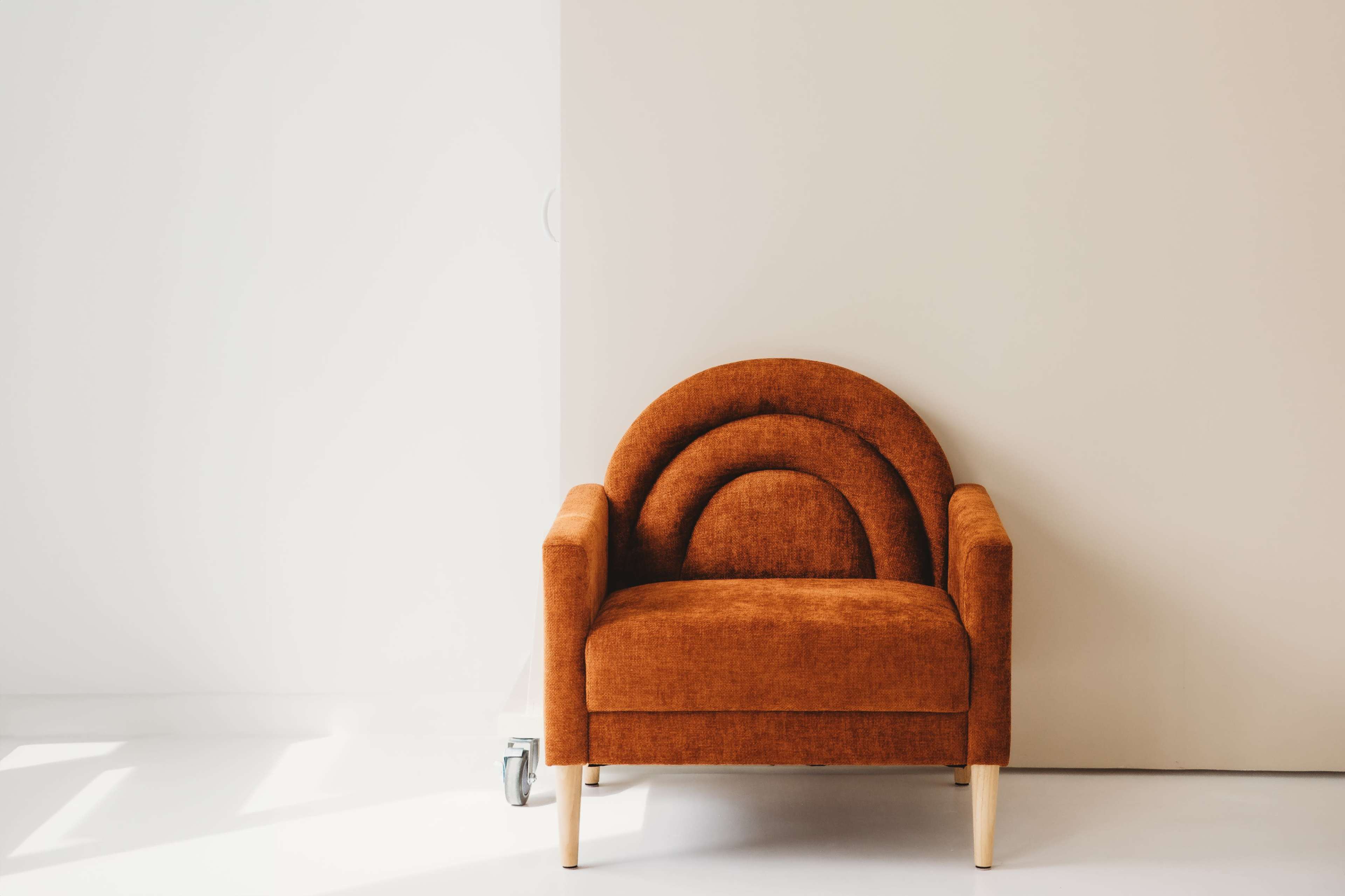 A textured orange armchair is positioned against a pale beige wall in a minimalist space.